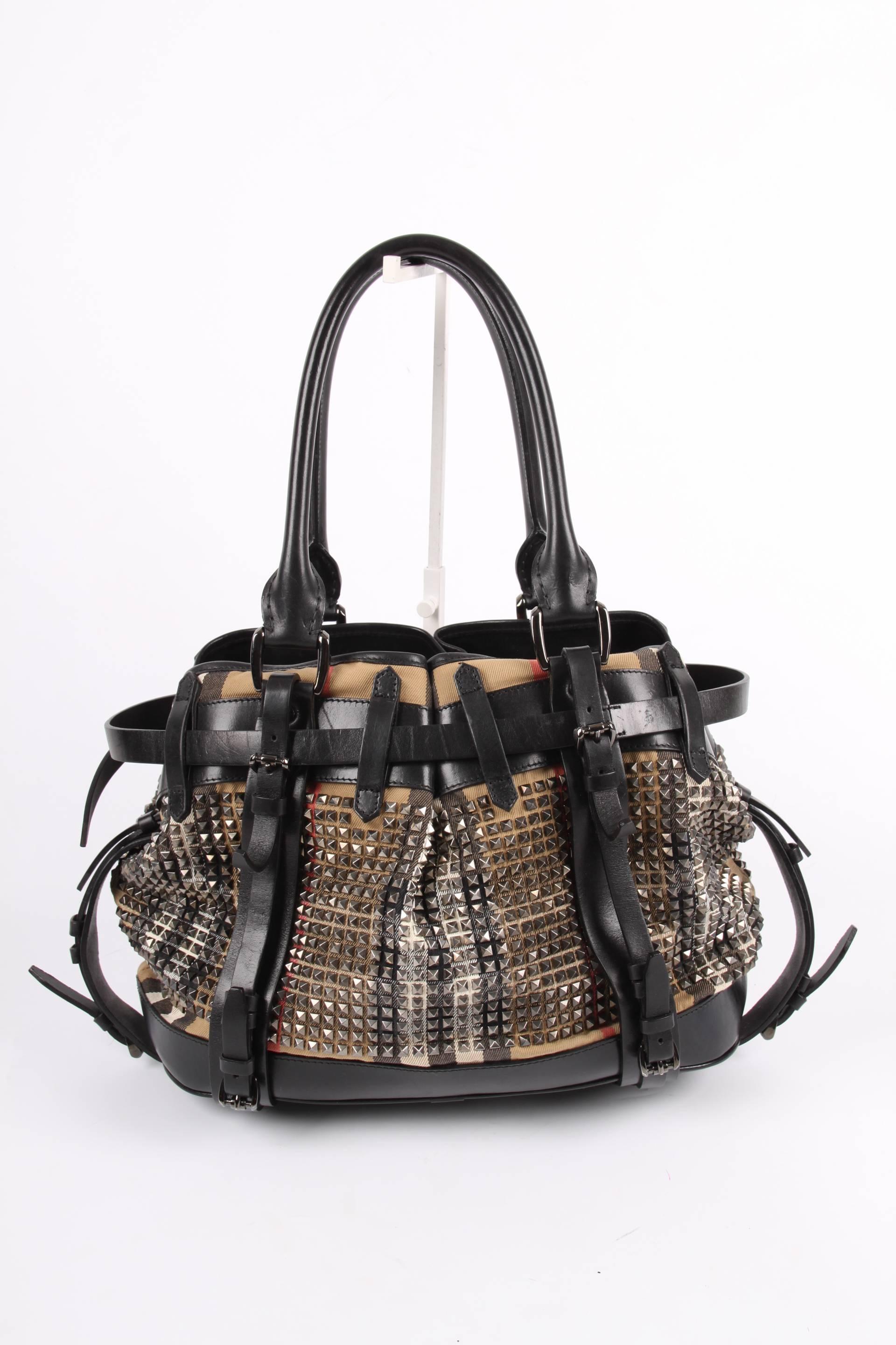 Rather large sized bag crafted in canvas with the welknown Burberry check in beige, black, white and red, covered with hundreds of silver-tone studs.

Combined with black leather, numerous decorative leather straps at the front plus a Burberry logo