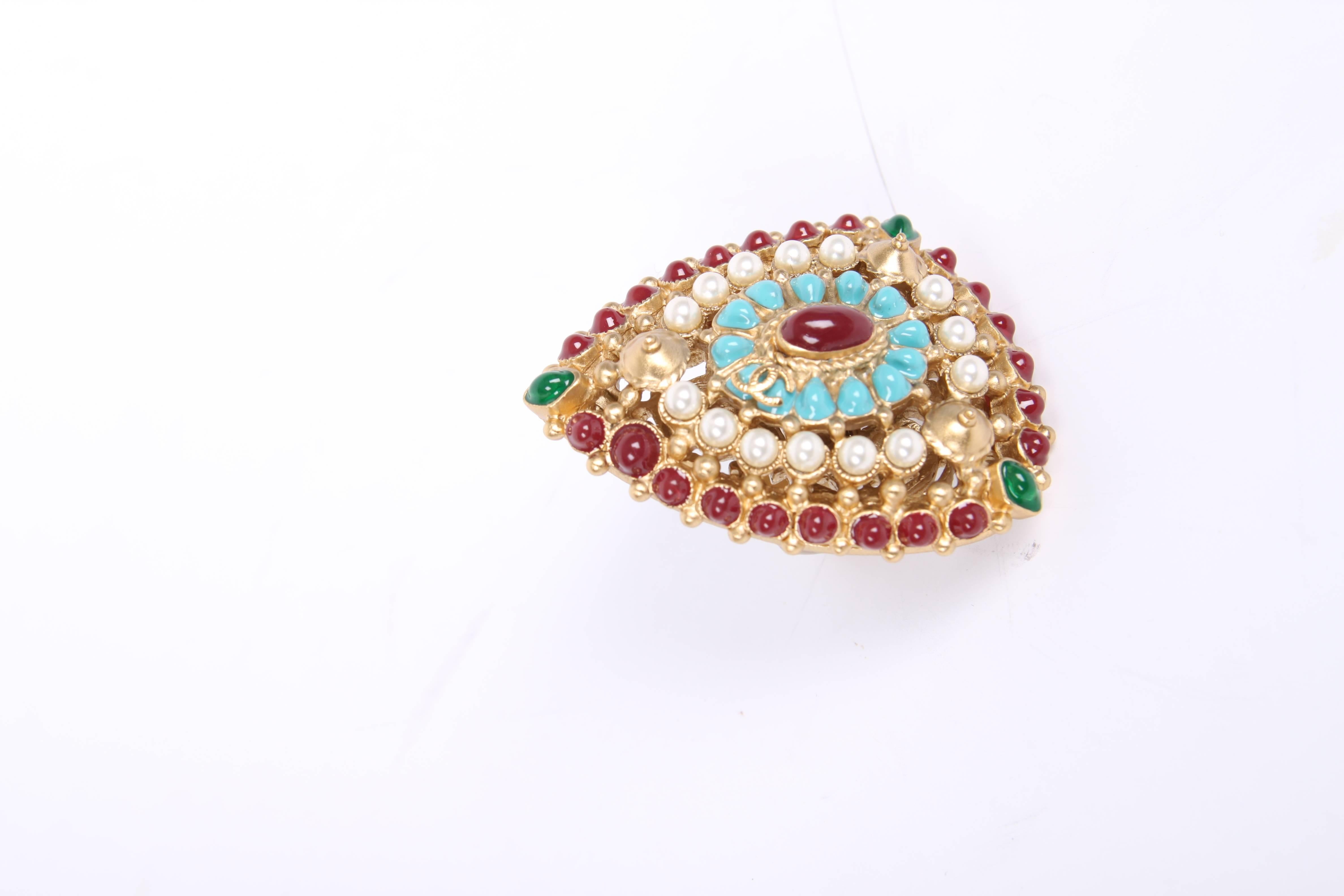 Chanel made this HUGE ring covered with pearls and dark red, turquoise and green gem stones.

A triangle shaped model, a large oval red stone in the center surrounded by turquoise stones with a gold-tone interlocking CC logo on the right. Perfect to