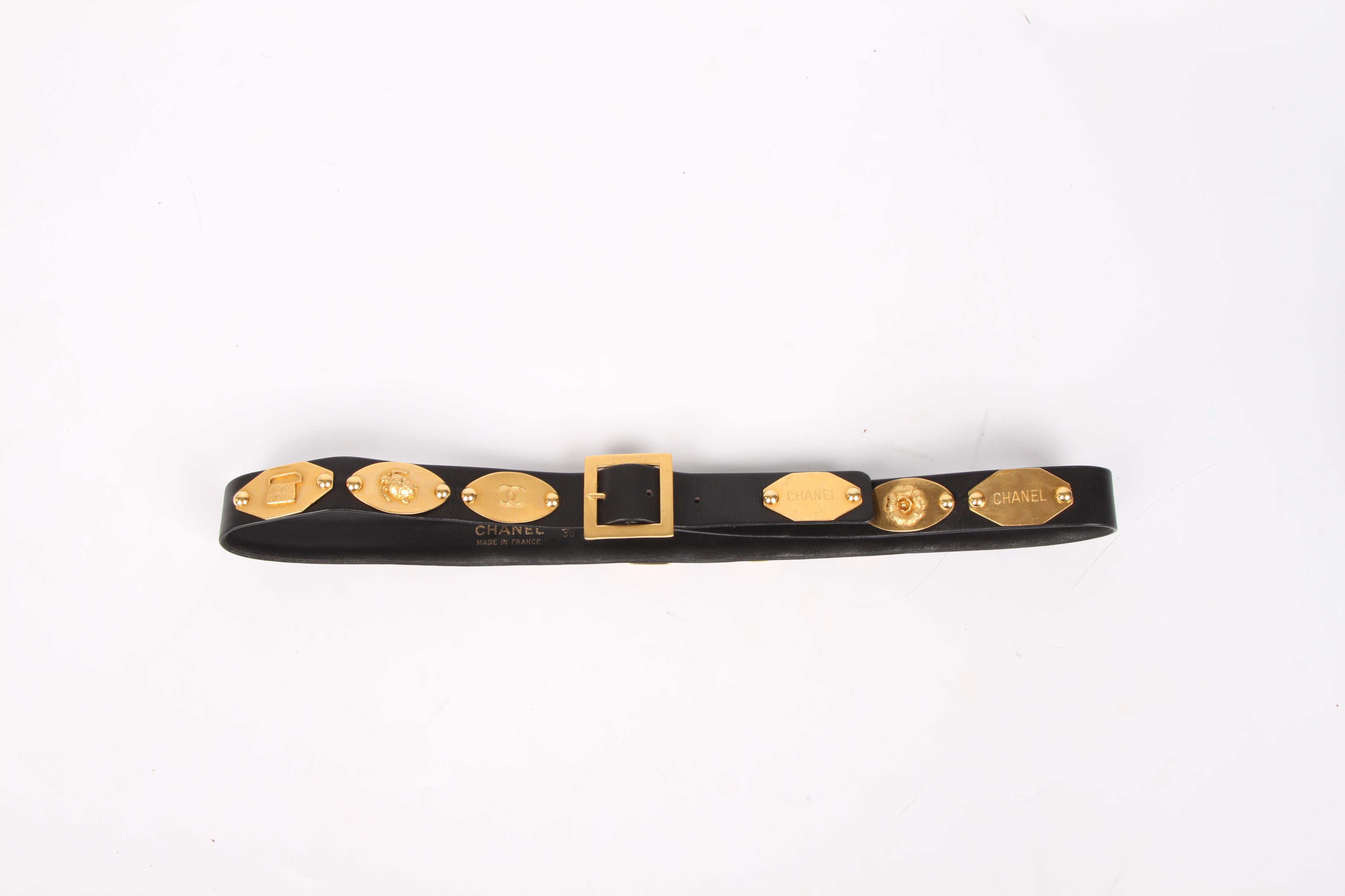 Skinny black leather belt by Chanel covered with logo plaques in different shapes. Vintage!

As much as tien gold-tone plaques have been attached to the belt with different images; a turtle, a four leaf clover, a bag, a perfume bottle, a camellia