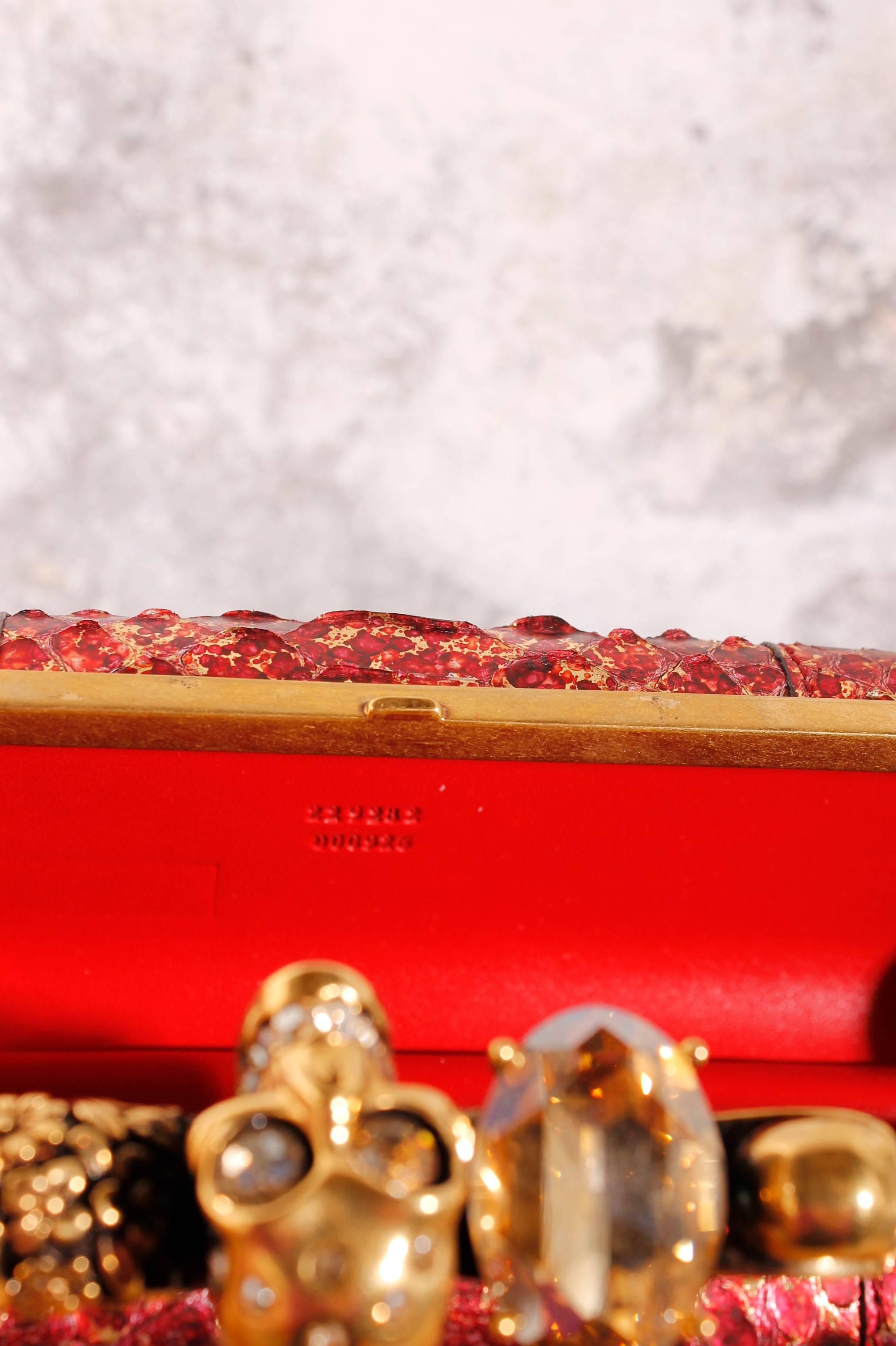 The famous clutch of Alexander McQueen! This one is made of python leather in red golden metallic. 

The hardware is in gold with an 'antique finish' which gives a nice contrast. The four rings on top are used as closure and are all different. One