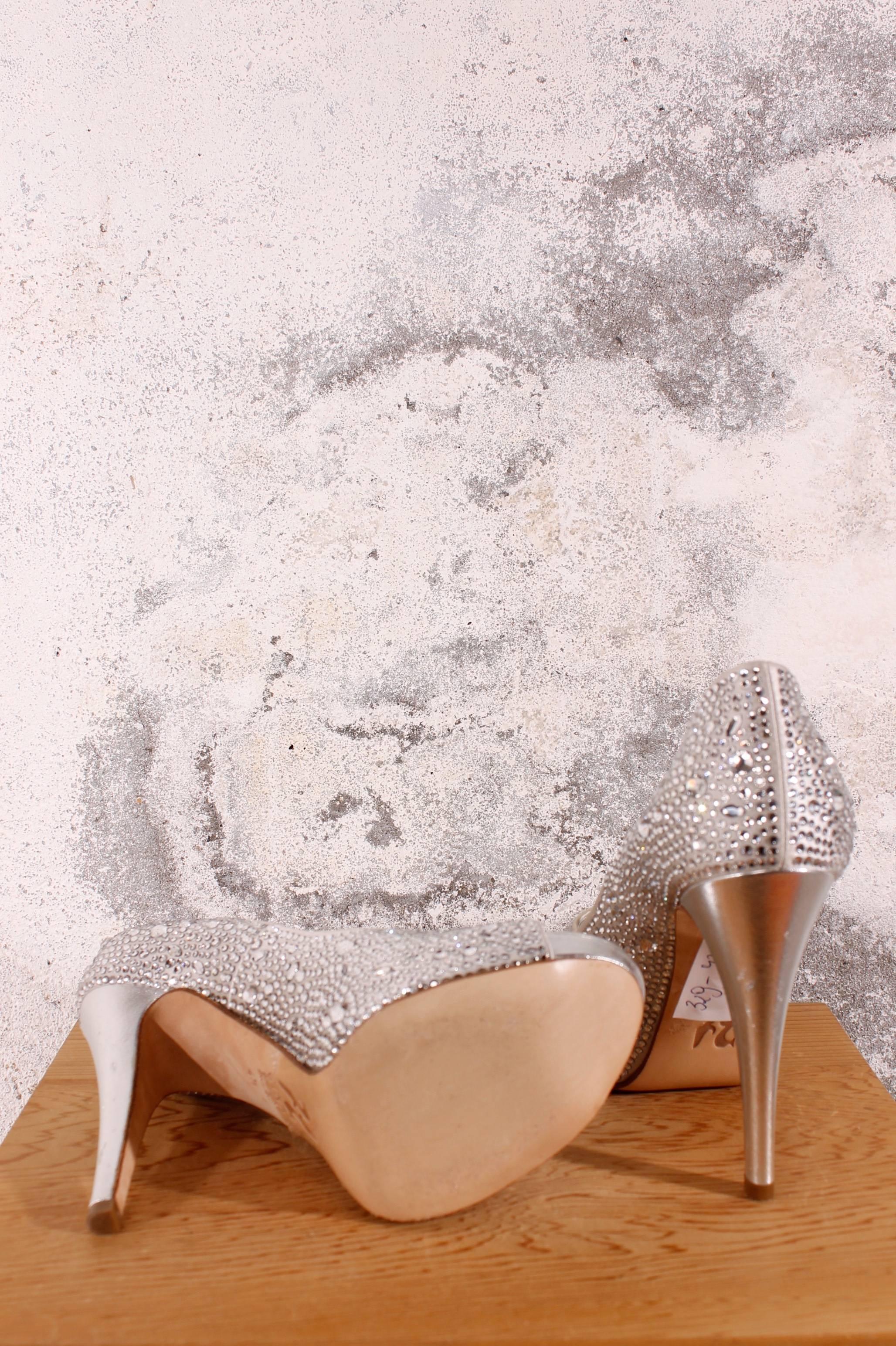 Gina Pumps find their origin in England, beautiful!

This shiny pair has white coloured crystals in different sizes and shapes all over the shoe. The base is made of silver coloured satin lined with leather, also in silver.

The heel is alsmost