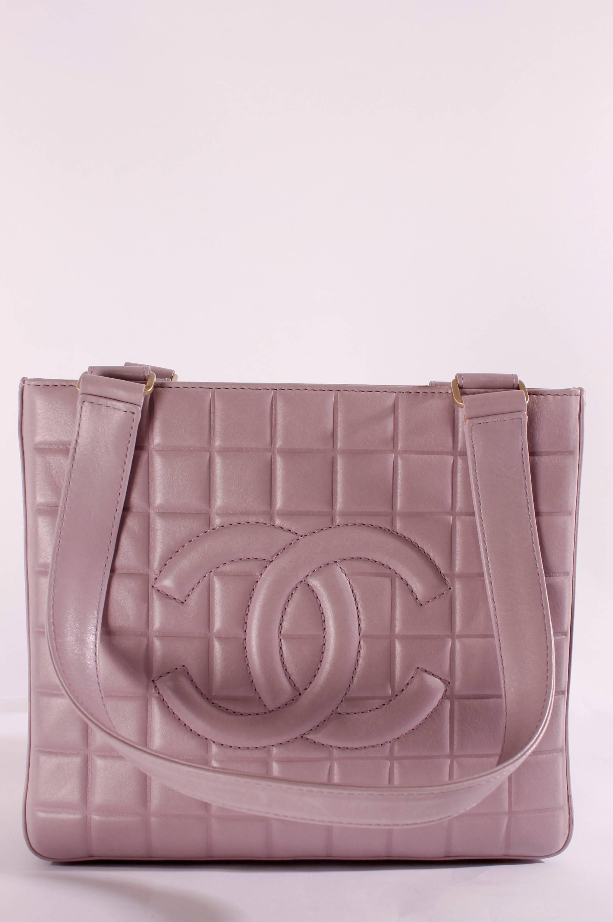 Nice and square lambskin leather handbag made by Chanel in 2002, the color is very light lavender.

This bag closes with a matte golden zipper on top with a CHANEL-dangle hanging down from it, the hardware on the straps is also in matte