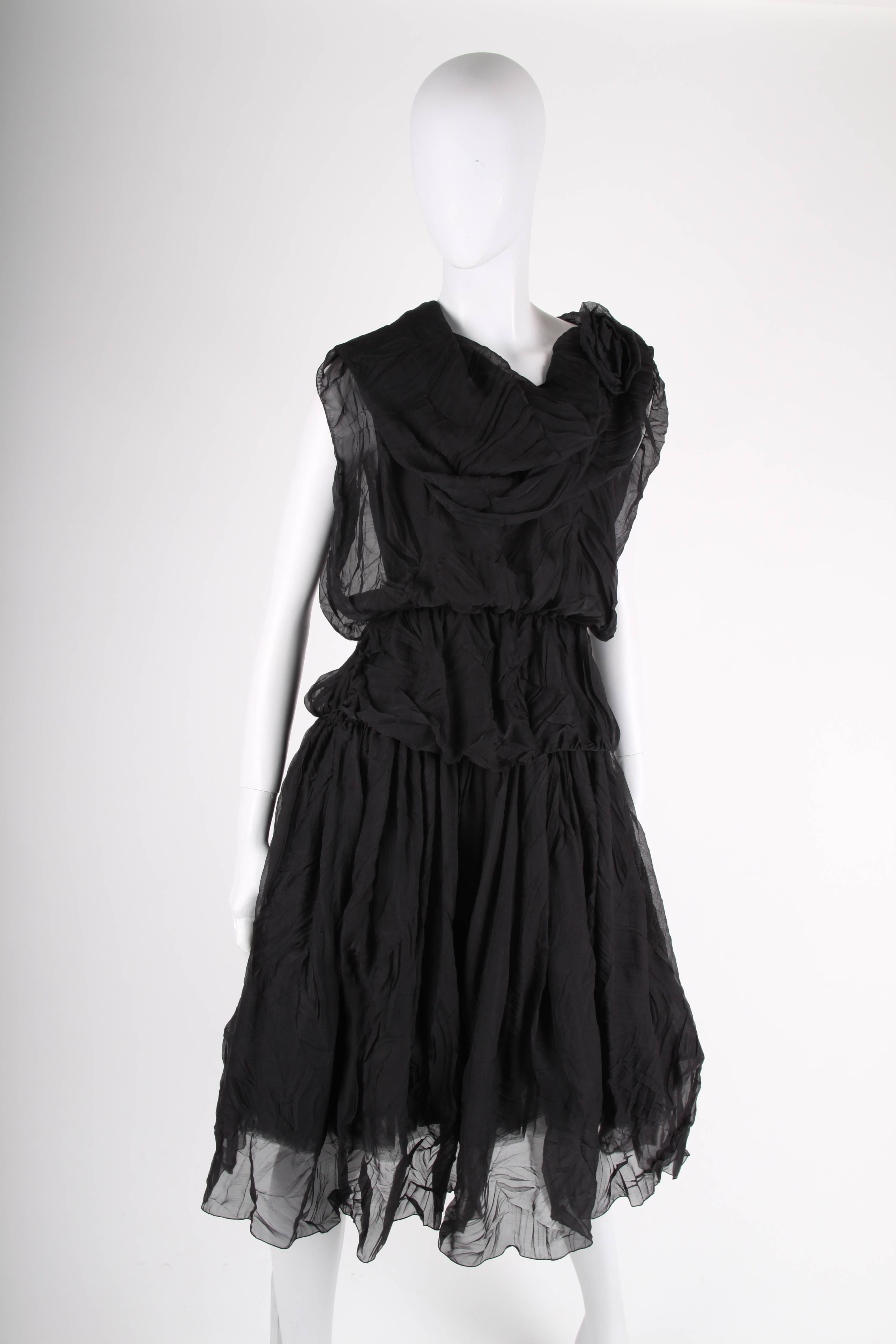A silk beauty from the Chanel fall collection of 2000.

Sleeveless black dress with a round neckline and multiple layers of wrinkled silk. A camellia corsage on the left shoulder. Zip closure on the back. Underneath the wide skirt you will find a