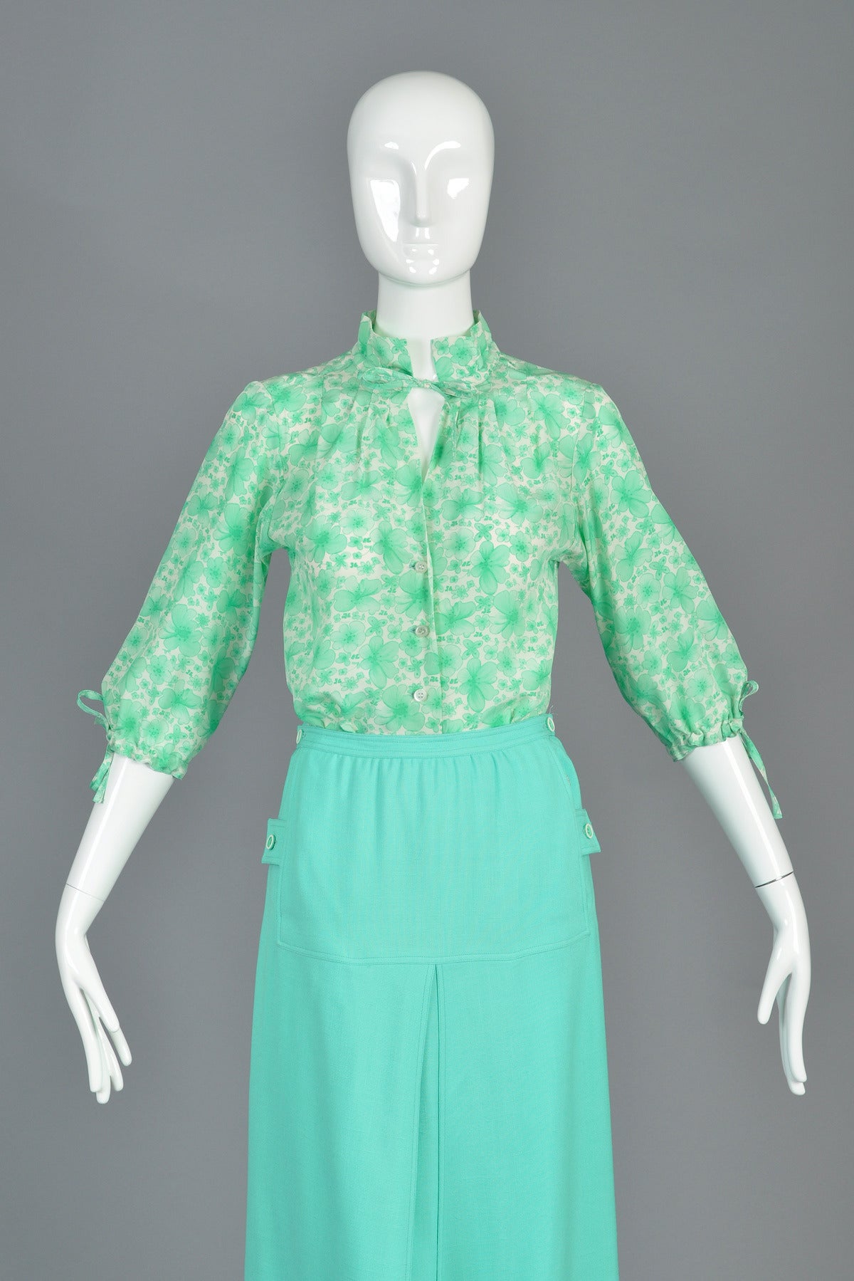 Darling vintage 1970s silk blouse by Andre Courrèges. Green all-over floral print with tiny Courrèges logos. Three quarter bloused sleeves with wrist ties. Ruffled collar with tie at neck. Button front. Excellent condition — unworn with original