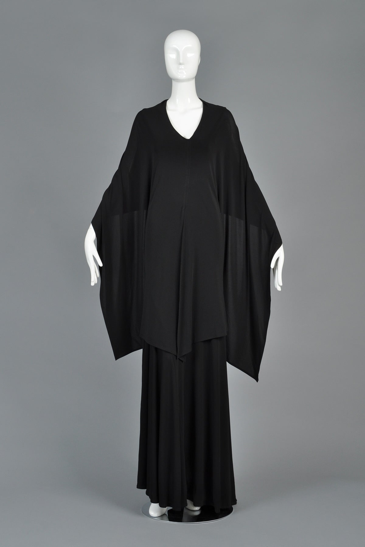 Lovely recent black caped dress by Eun Hwa. Dress is made from slinky black jersey with a plunging neckline and flared skirt. The attached cape/shawl can be worn multiple ways - thrown over the shoulders, as a scarf or even as a hood. Has two hidden