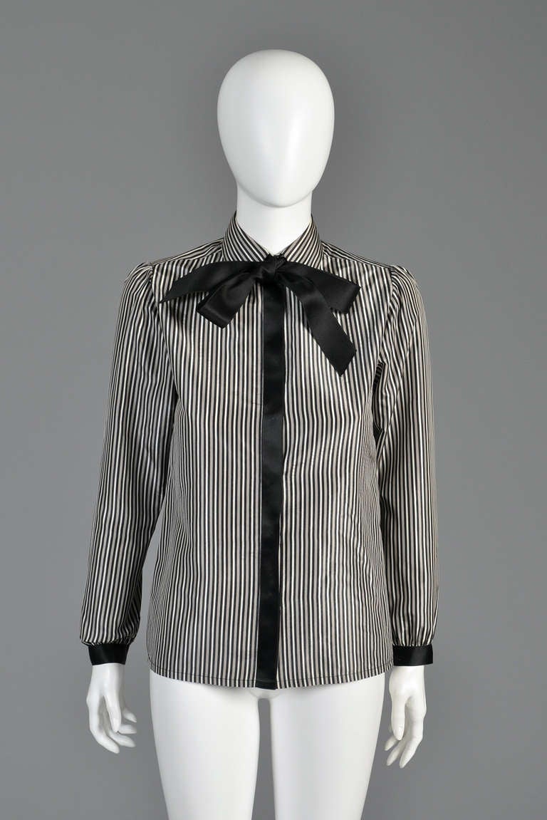 Beautiful vintage Chanel pinstriped blouse with ascot. 100% silk with tiny black, grey + cream pinstripes. Black silk ribbon runs up the placket + around the cuffs and is mimicked by the attached ascot. Ascot can easily be removed with a seam