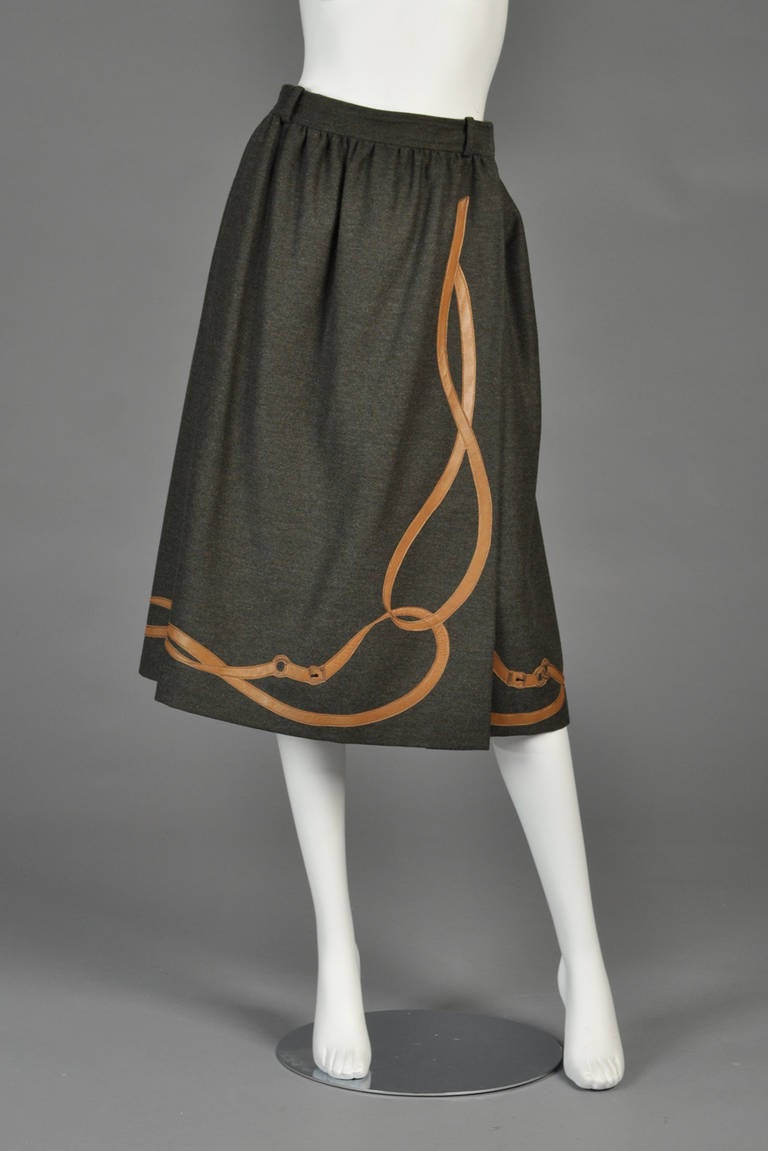 Lovely 1970s Gucci wool + leather skirt. Dark charcoal grey heavy wool with ultra high waisted a-line wrap construction and applied leather bridle motif. Sought after, collectible piece. Green silk Gucci monogrammed lining. 

Excellent vintage