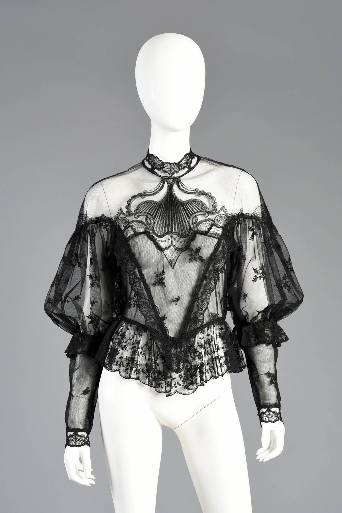 Un'irreale camicetta vintage anni '70 in pizzo trasparente. Maniche a sbuffo enormi con polsini extra lunghi. Bellissimo pizzo a rete femminile con accenti floreali. Peplum svolazzante. Carré ornato con volute e pannelli ritagliati. Chiusura con