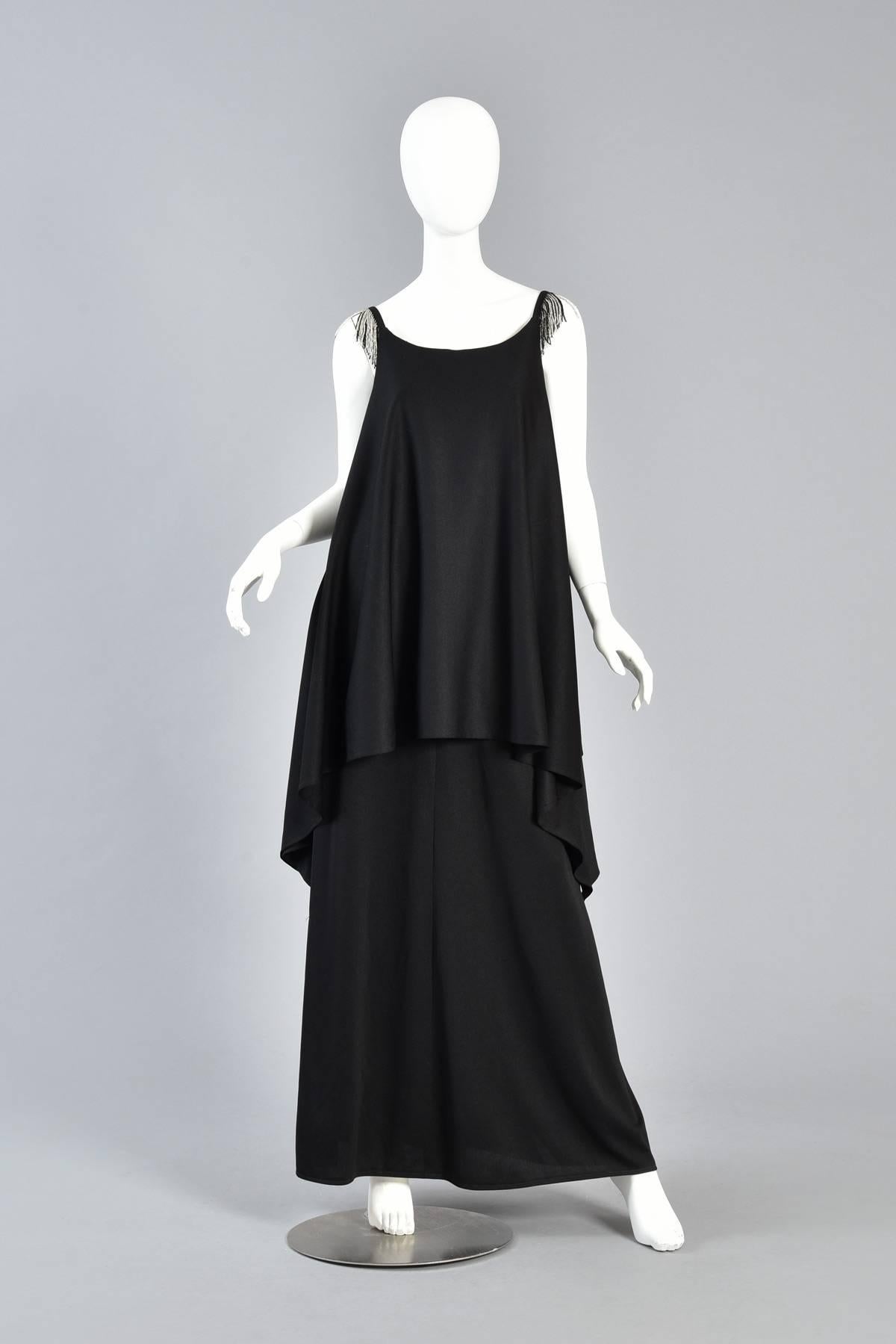 Simple & chic 1970s tiered evening gown. Heavyweight black jersey with high scooped neckline gives way to a flattering tiered & draped gown. We love how the top tier hangs longer on the sides! Also features beaded fringe shoulders for that little