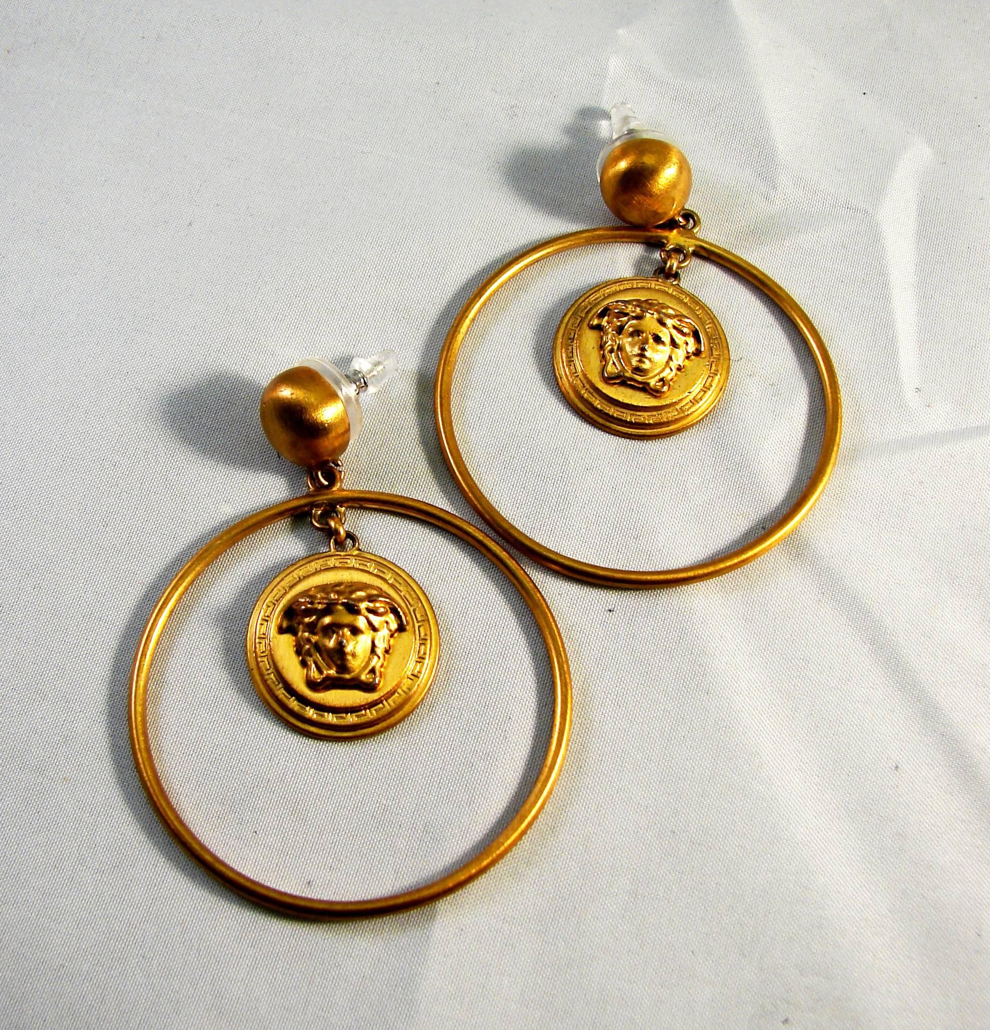 Gold hoop earrings feature Versace's signature Medusa head in the center.  Measure 2