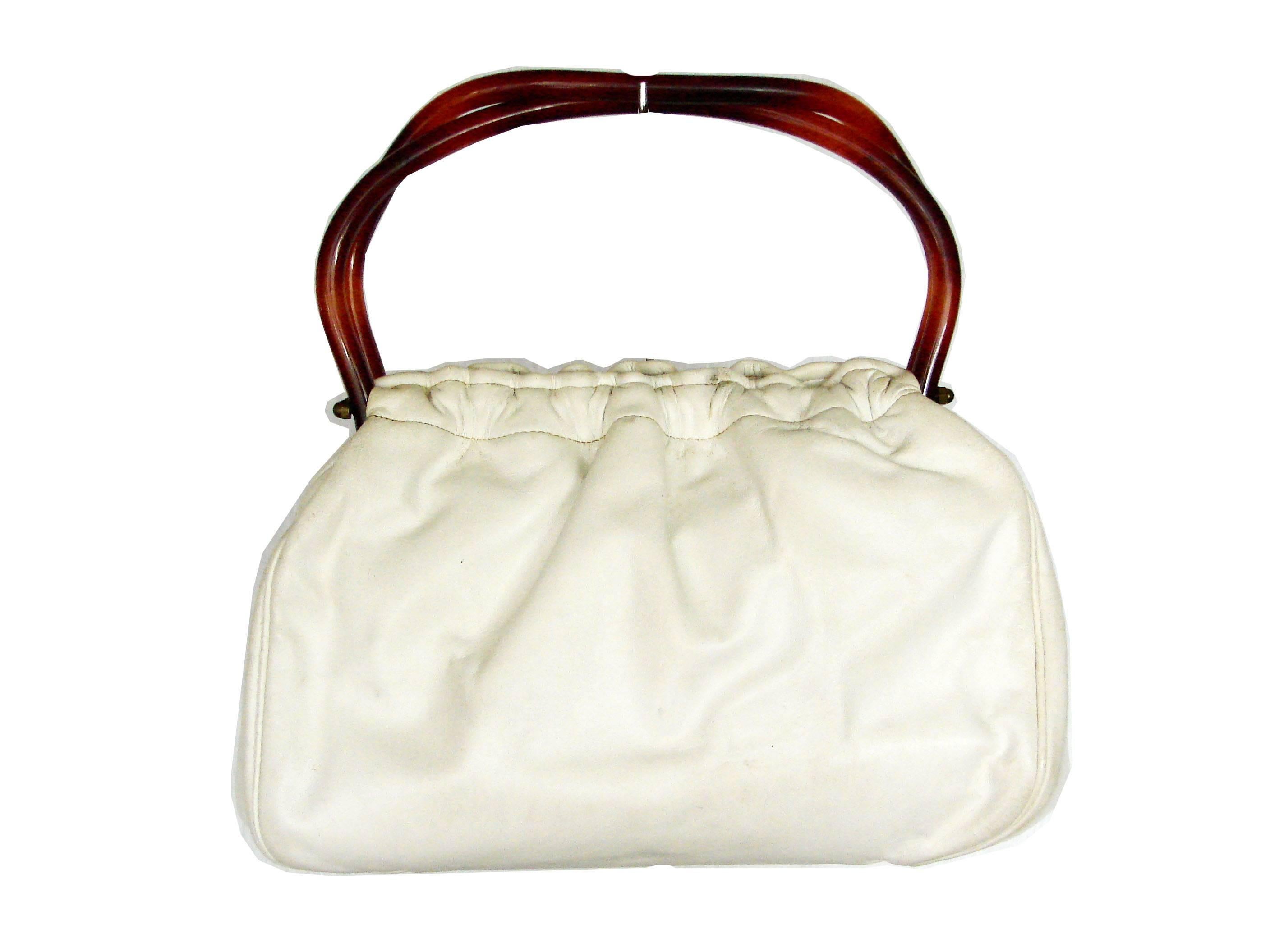 Here's a cool leather handbag from Morris Moskowitz, made in the 1960s.  Fully lined in fabric, it features one small zip pocket.  In very good condition overall, we note several rubs to the white leather, and darkening to the leather from the brass