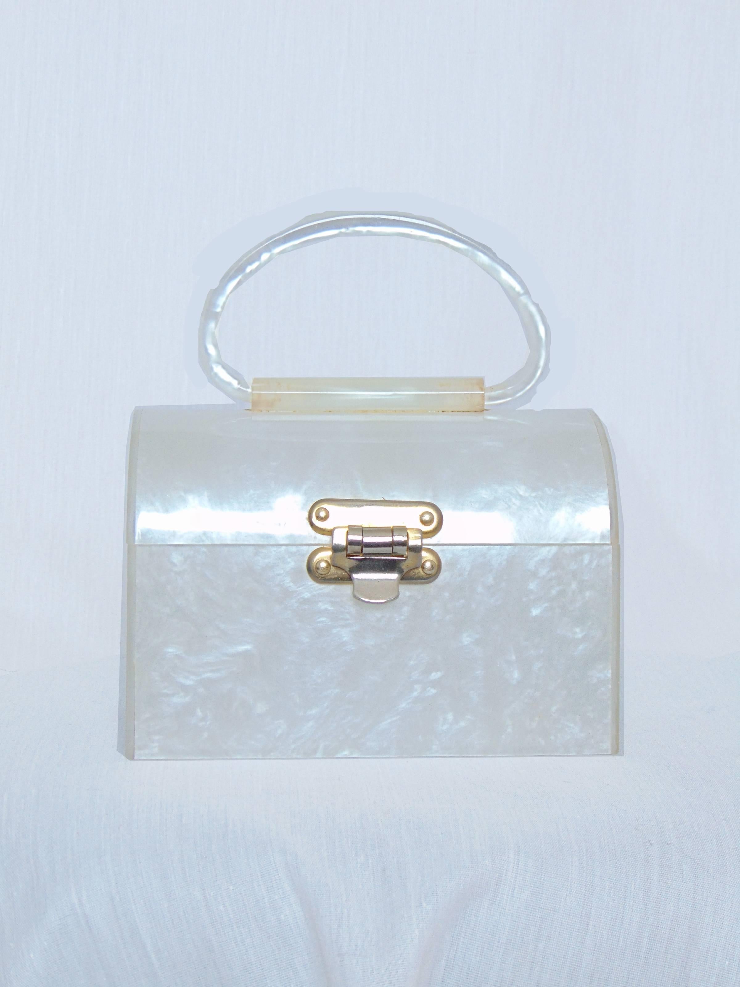 Here's an adorable little bag from the 1960s. Made from a white Lucite resin, it measures 6.25in long x 4.25in high x 4in deep with a 3in handle drop.  In very good condition for its age, we note some yellowing to the handle base, patina to the