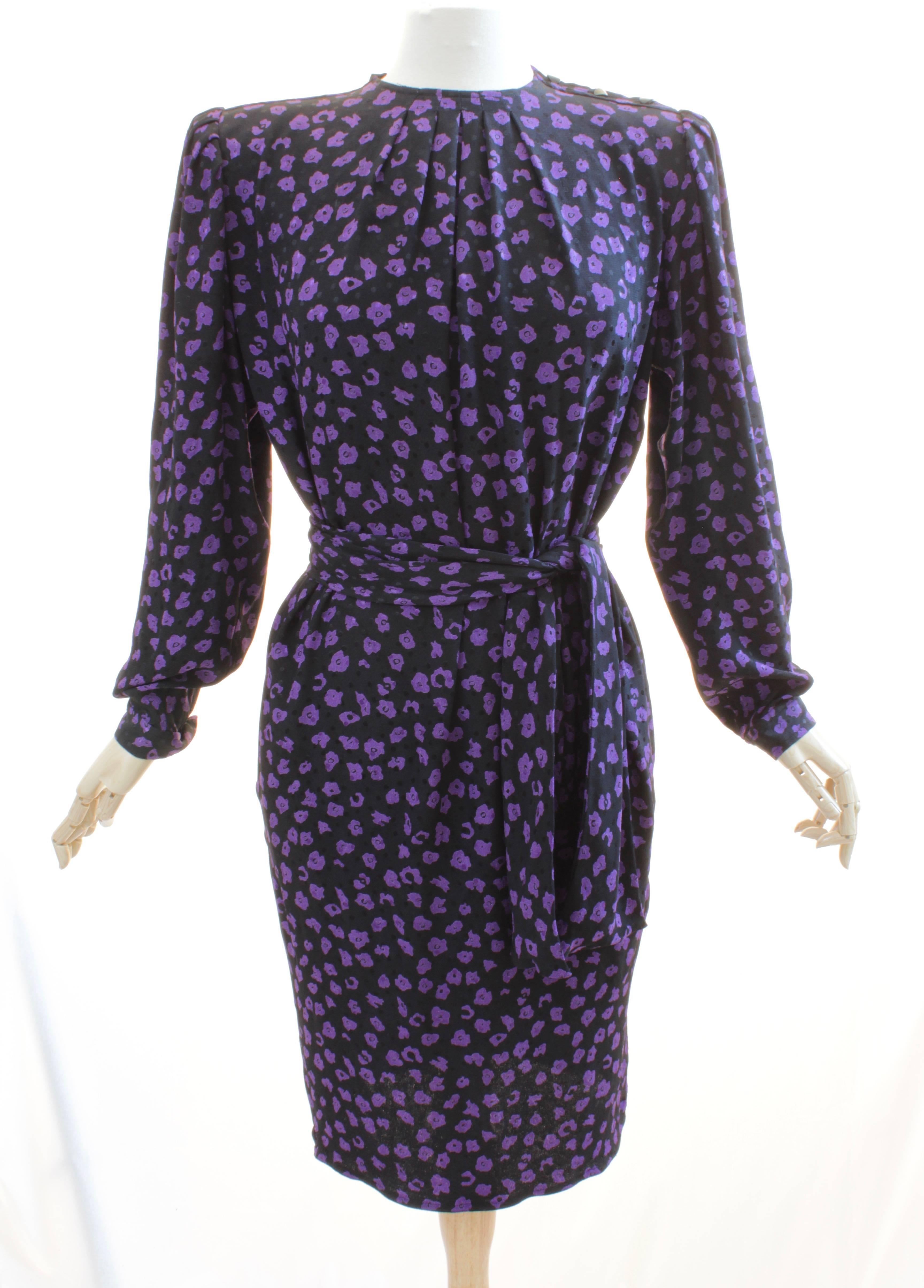 This pretty belted silk dress was made by Ungaro, most likely in the early 1980s.  Made from a black silk jacquard fabric with purple floral motif, it's unlined and fastens with buttons at the wearers left shoulder. Comes with its matching and