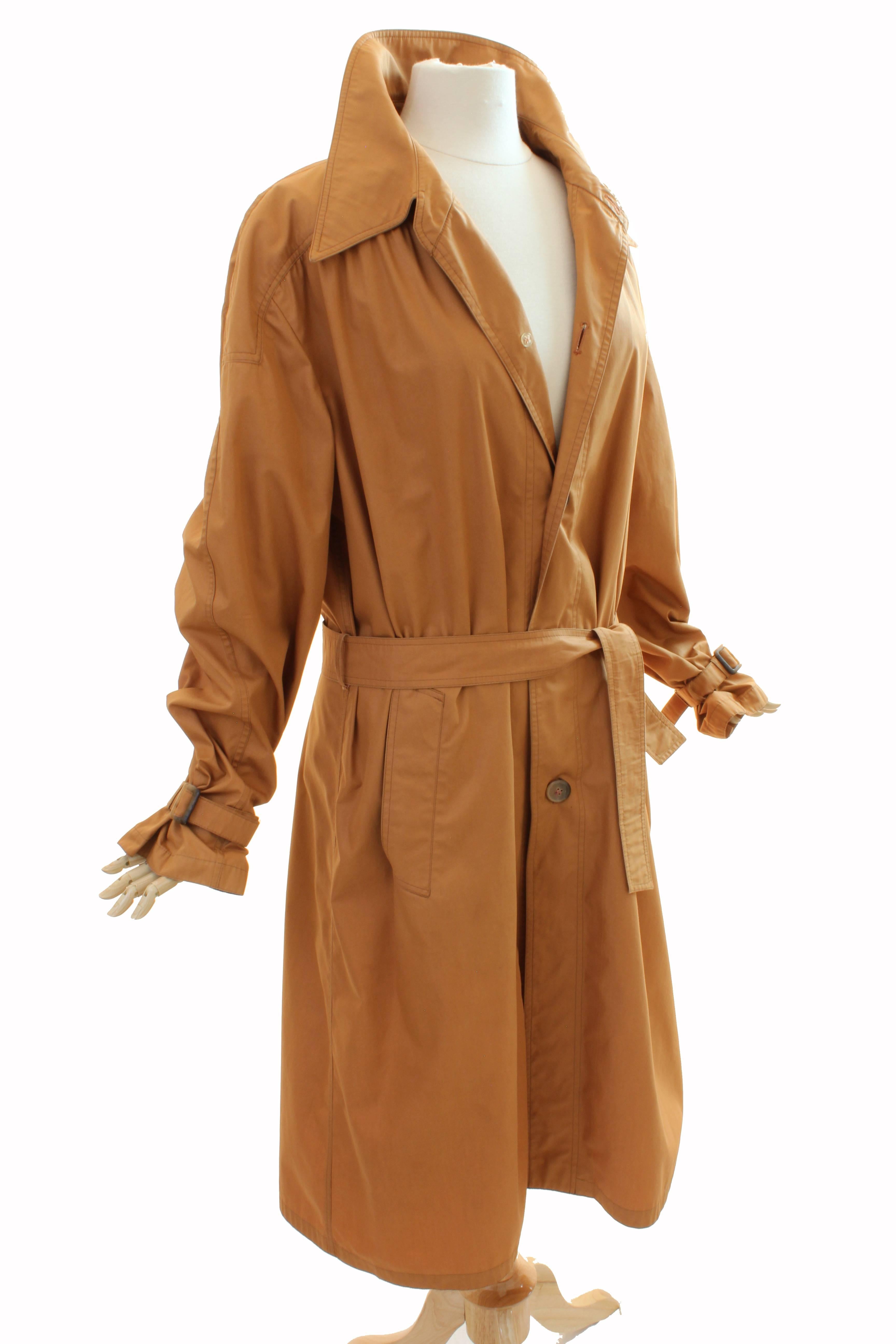 This chic trench was made by Liberty of London, most likely in the late 1950s.  Made from a cotton blend fabric in a deep shade of camel tan, it features side pockets, cinch buckles at the sleeve ends and a wrap-tie belt.  Unlined and lightweight,