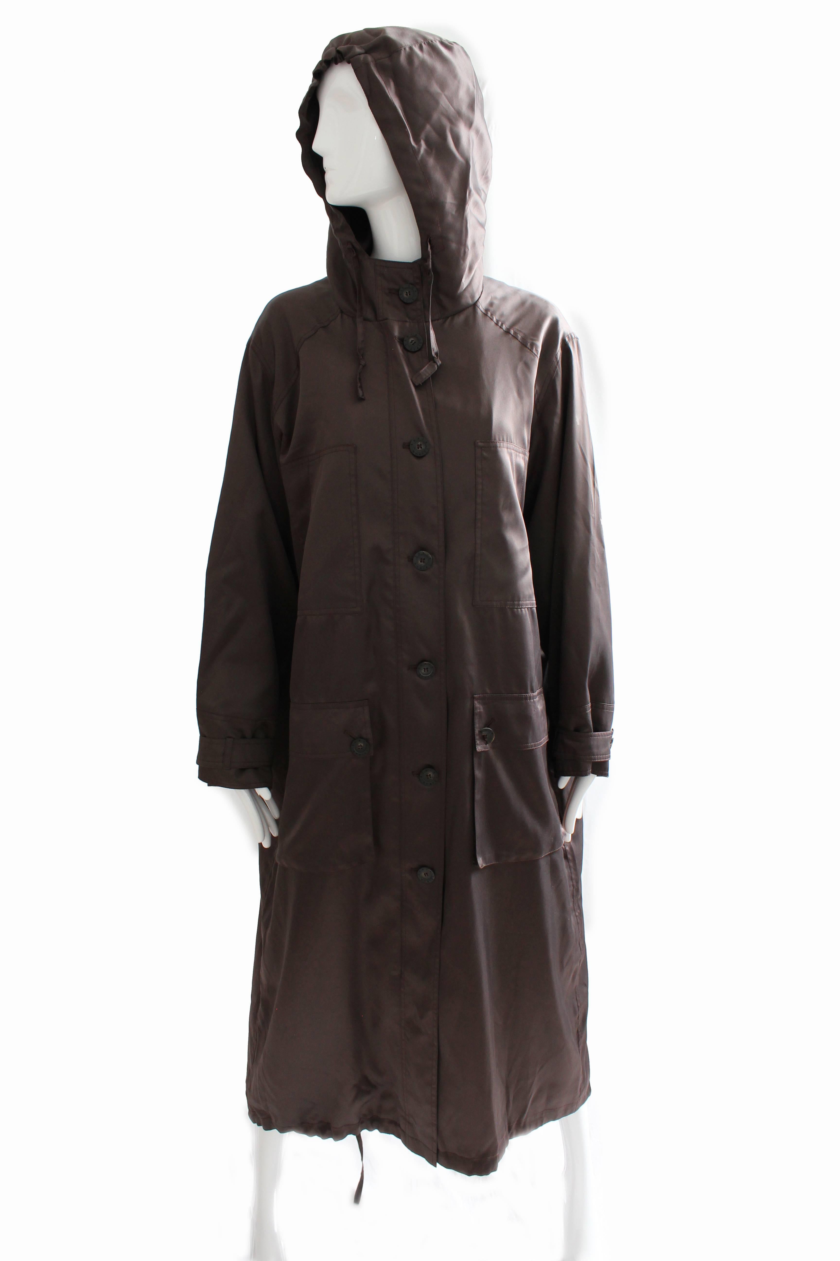 This chic trench coat was made by Sonia Rykiel, most likely in the early 1990s.  Made from a deep brown satin, it features an attached hood, zippered front with button overlay, and large button square pockets at each hip.  The bottom hem features a