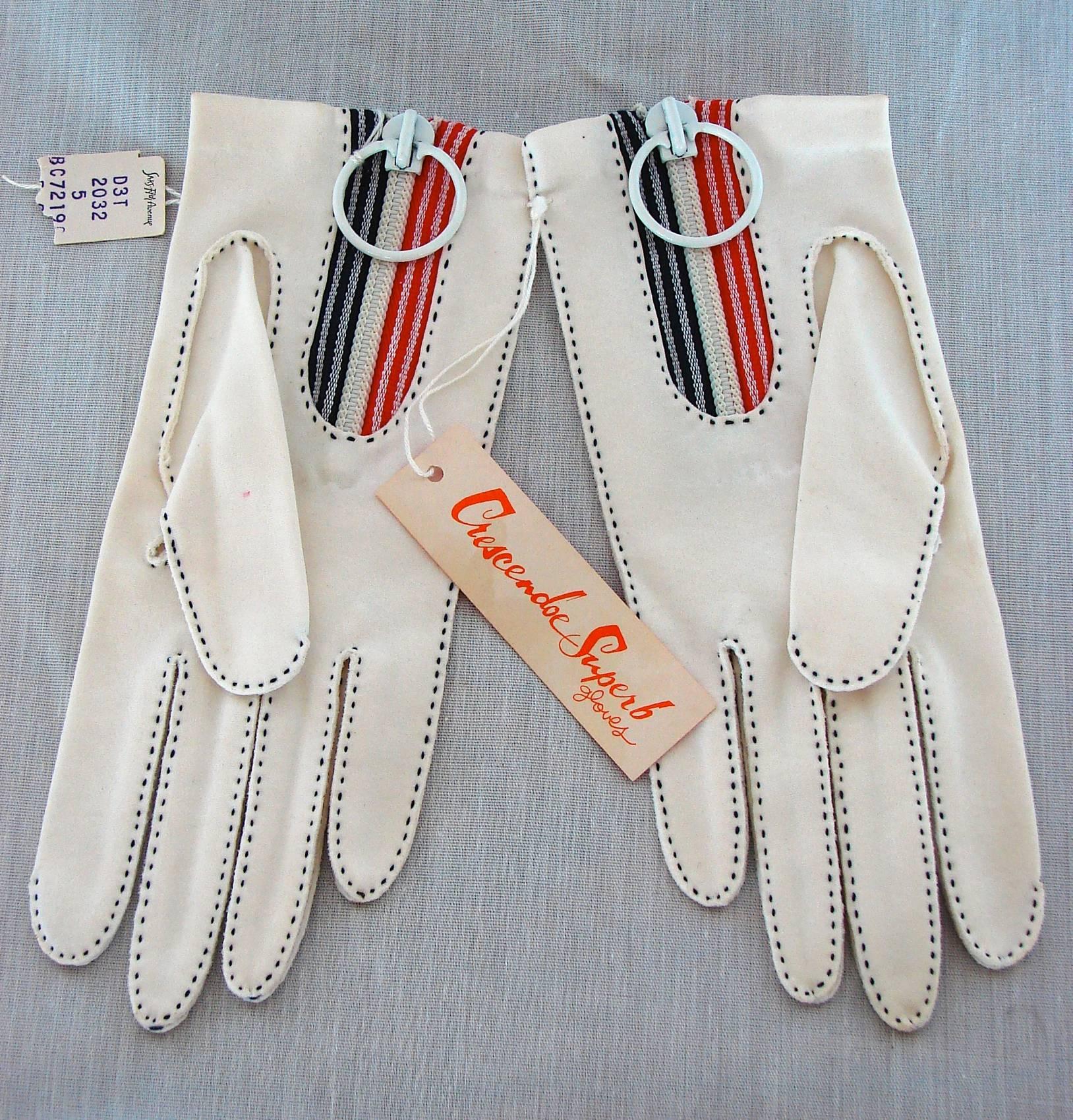These mod white cotton gloves were designed in the late 60s or early 70s by Bonnie Cashin for Crescendoe.  They feature contrast navy stitching and a red, white and navy striped wrist area with a chunky white zipper and super mod 