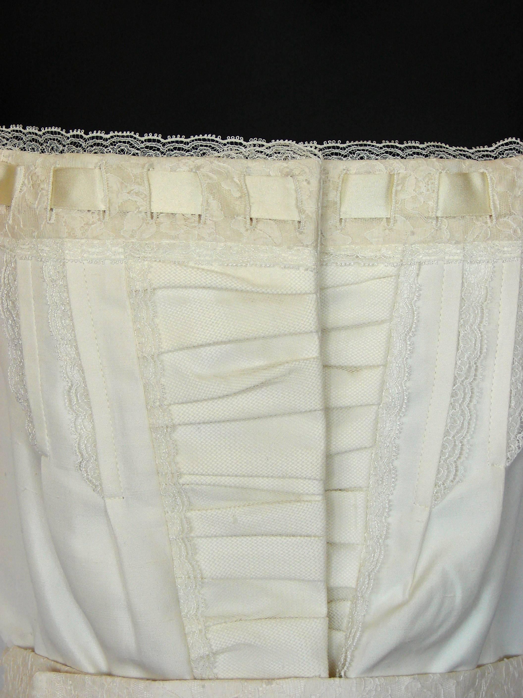 This lovely white corset top was made by Christian Dior in the early 2000s.  Made from what we believe is cotton fabric (no content tag), it's trimmed in silk satin and lace on the bodice.  Fully-lined, this piece has boning at the sides and fastens