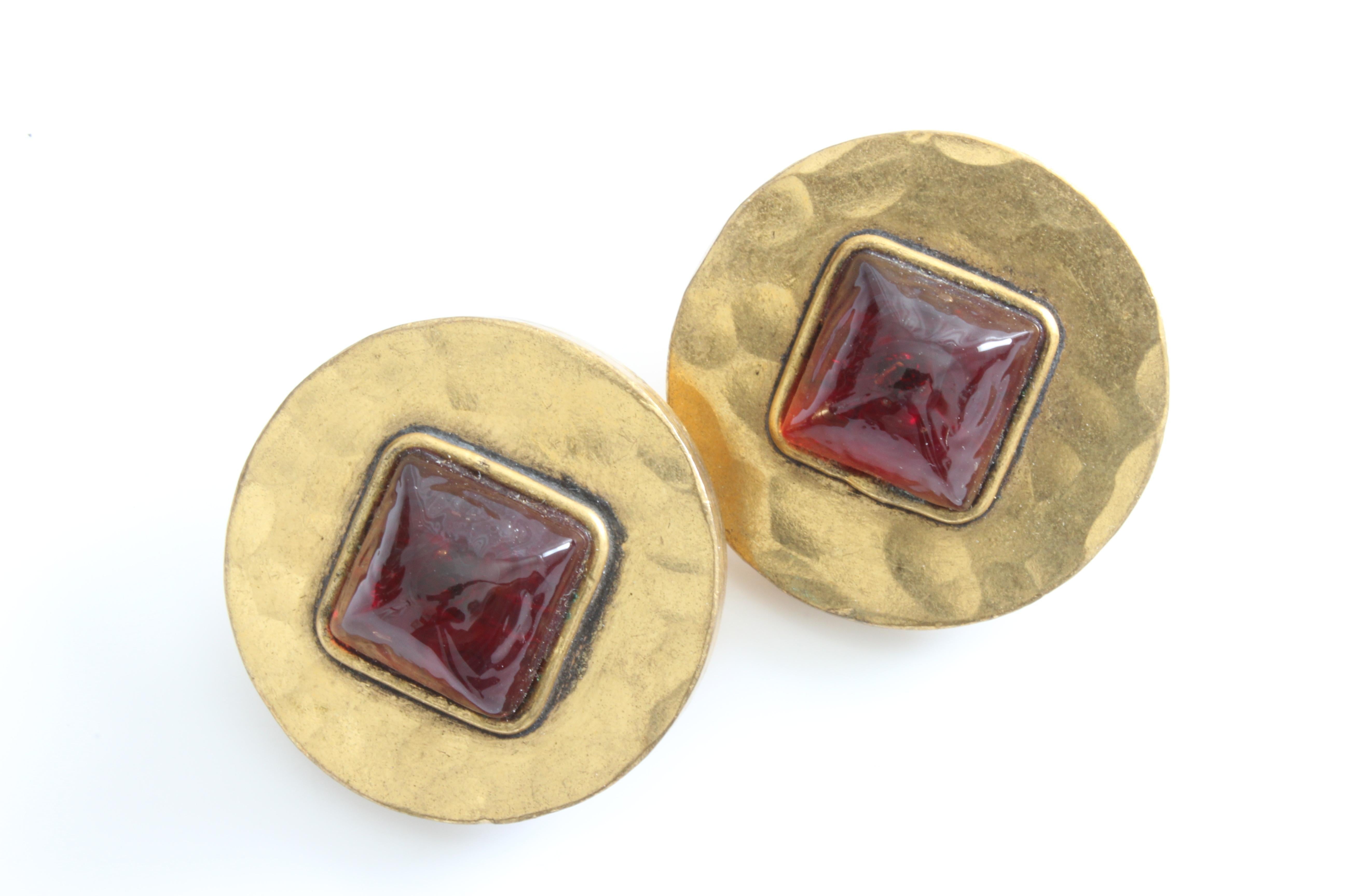 Here's a pair of earrings from CHANEL, likely made in the 1970s.  Made from hammered gold metal, they feature chunky dark red Gripoix centers and fasten clip style. In very good condition for their age, we note patina and scratching to the gold