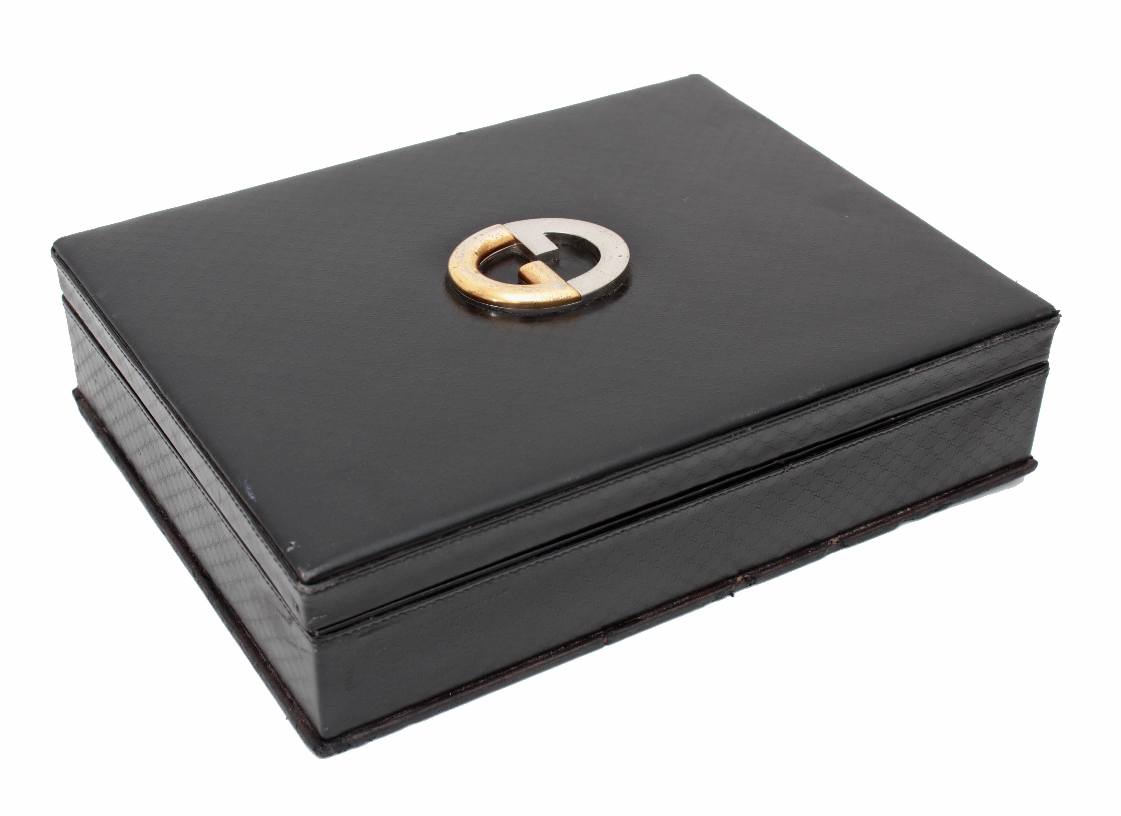 This vintage game case was made by Gucci, most likely in the early 1970s,  Made from black leather embossed with their GG logo, it features the Gucci logo in gold and silver on top.  The interior is lined in green felt and comes with Gucci playing
