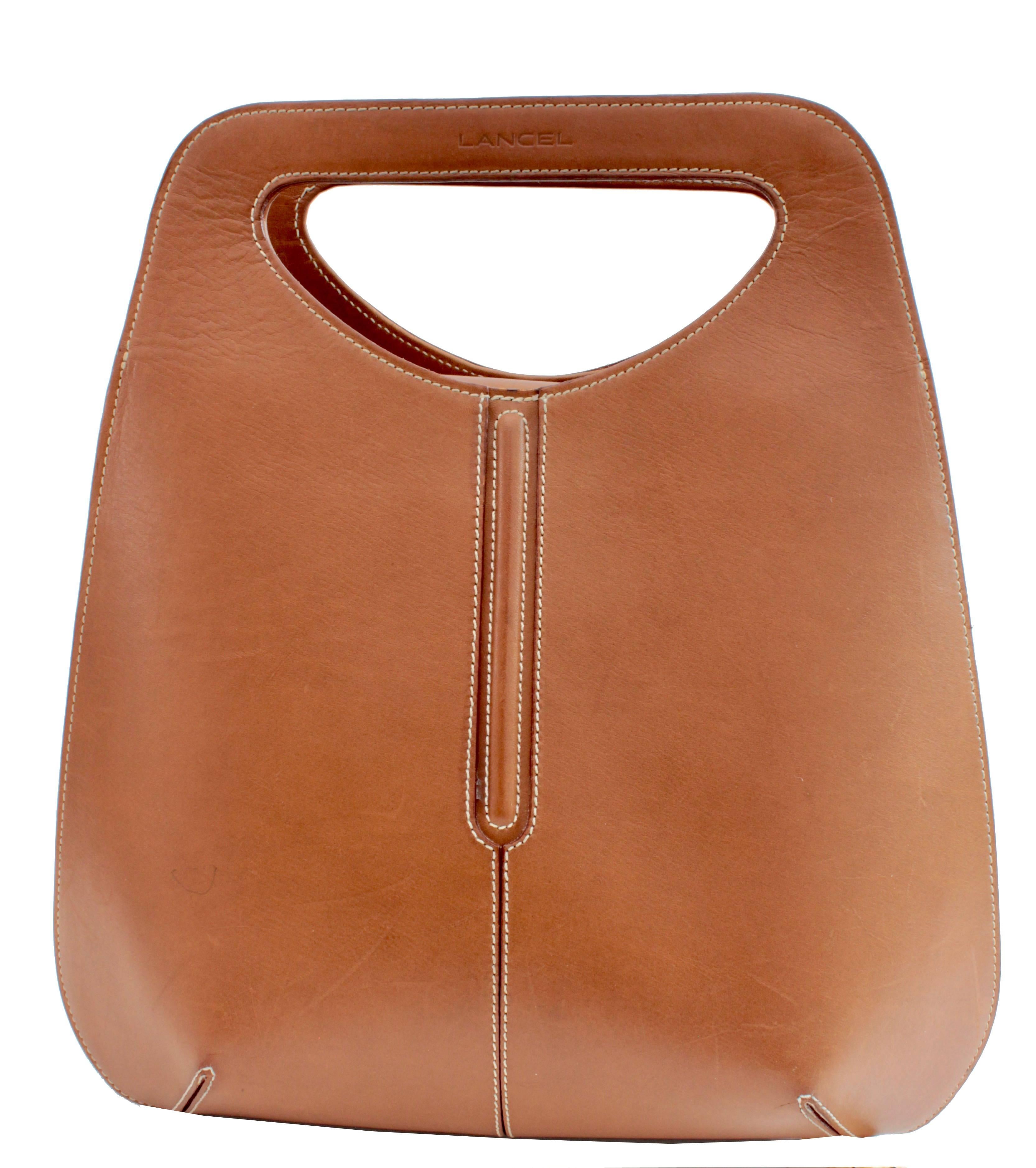 Here's a unique cut out handle tote bag from Lancel, most likely made in the late 1990s.  Made from saddle colored leather, this bowler shaped bag features white contrast stitching, a magnetic closure and is lined in cream canvas with one zipper