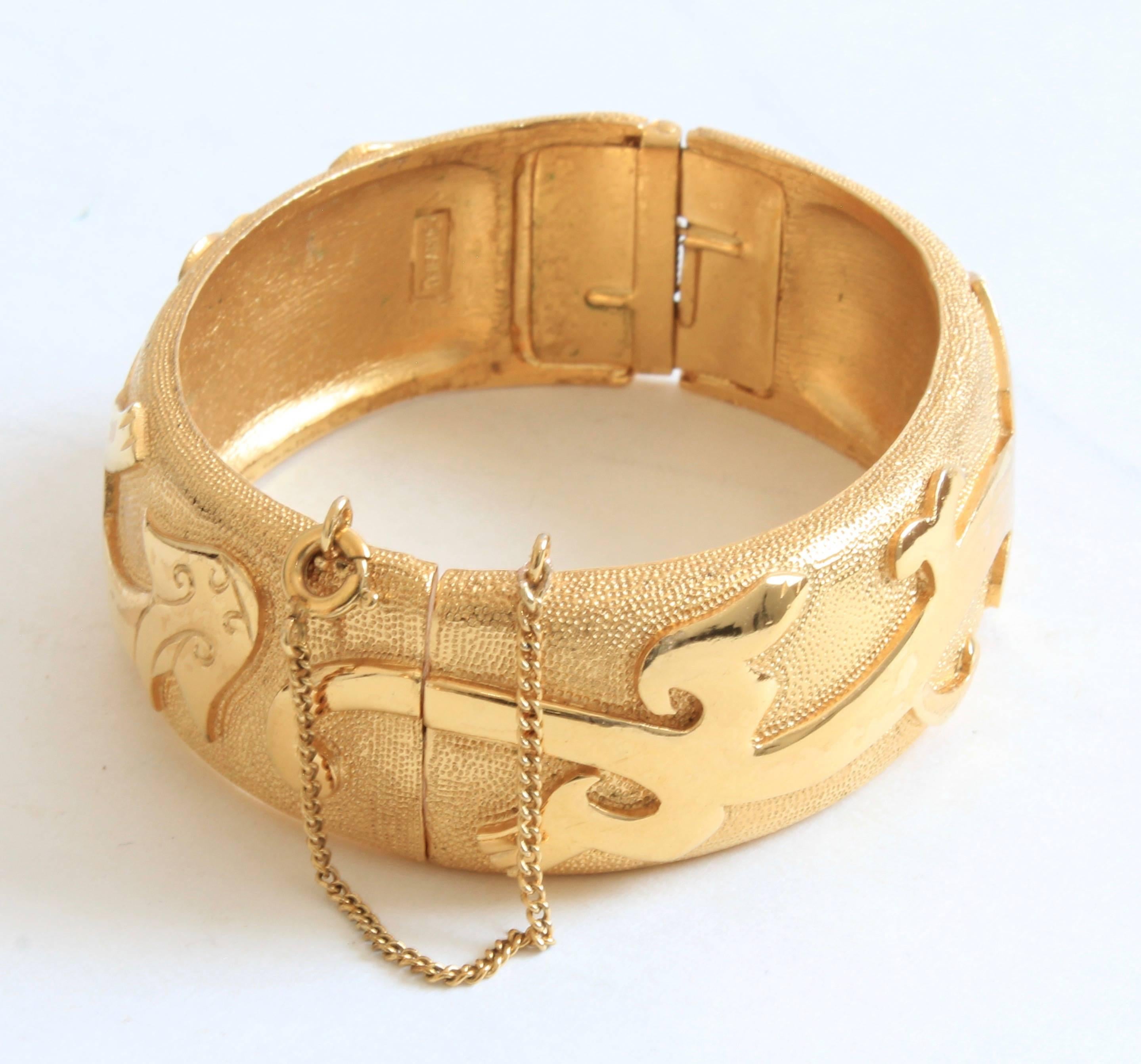 This unique hinged bracelet was made by Trifari, most likely in the 1960s.  Made from gold metal, it features a polished figural dragon motif against a textured background.  Features hinged construction with a safety chain catch, and stamped with