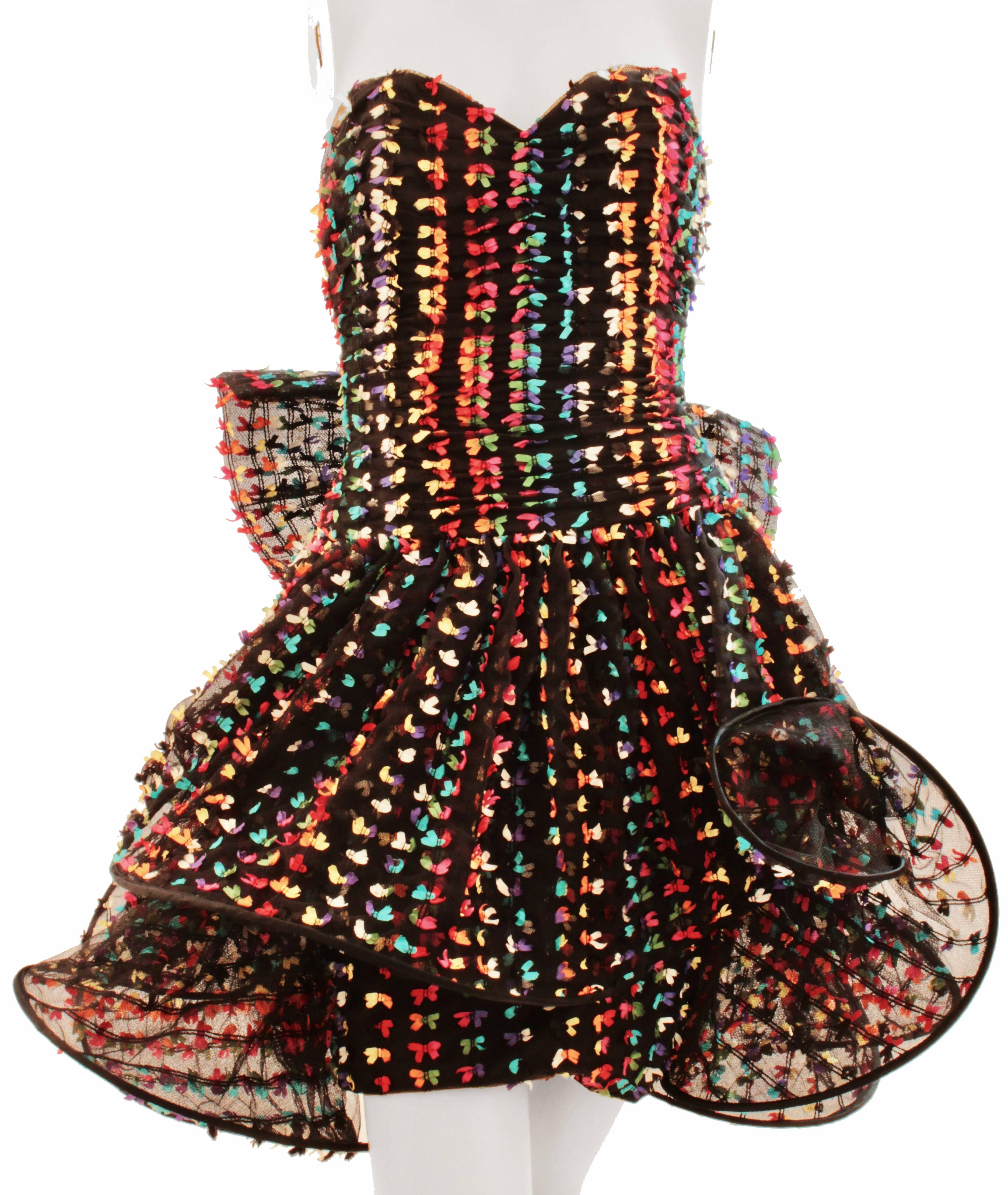This little cocktail dress was made by London designer Tomasz Starzewski, likely in the late 1990s.  Made from a black cotton blend mesh fabric, it features dozens of tiny confetti colored bows with a pliable hooped layer overlay at the skirt.