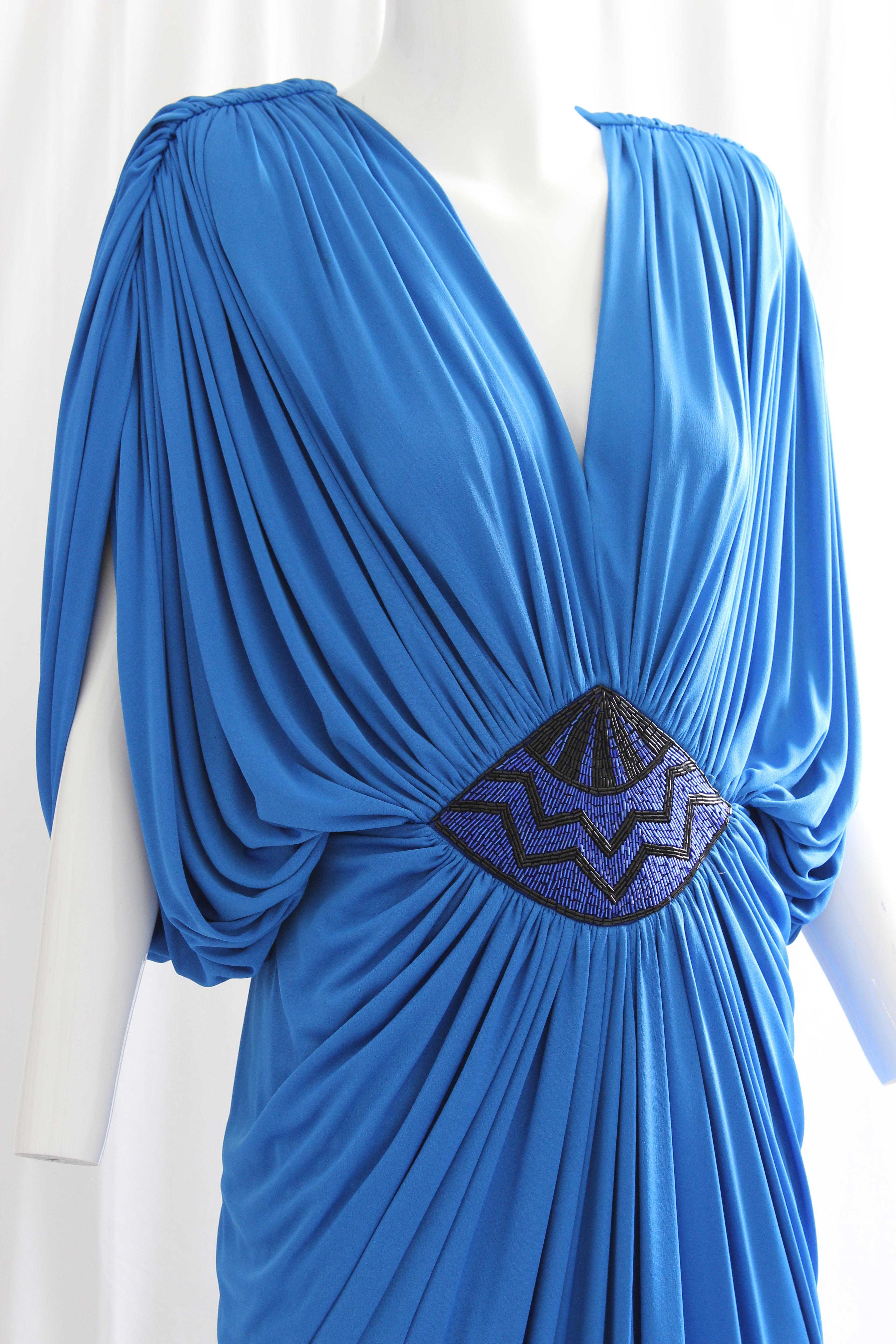 This fabulous evening gown was made by Tadashi Shoji, most likely in the early 80s.  Made from a cerulean jersey fabric, it features a draped batwing bodice with an embellished beaded panel at the waist.  In good condition given its age, we note