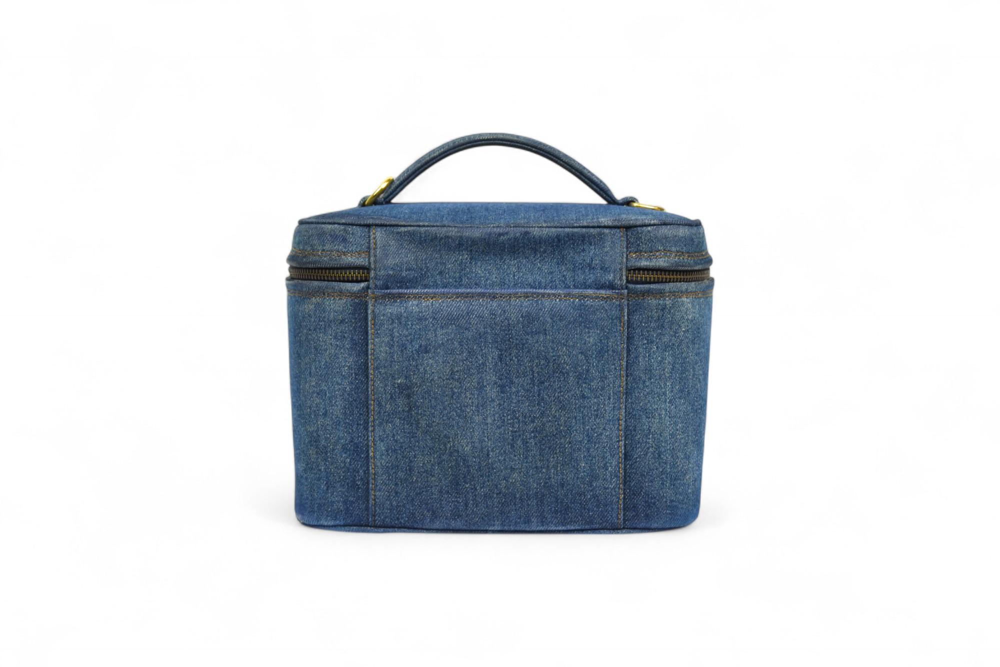 Confectionné dans un riche denim bleu et doté d'une silhouette structurée, ce vanity case de Chanel allie fonction utilitaire et mode de luxe. La forme carrée est accentuée par des coutures ton sur ton et une double fermeture à glissière, tandis que