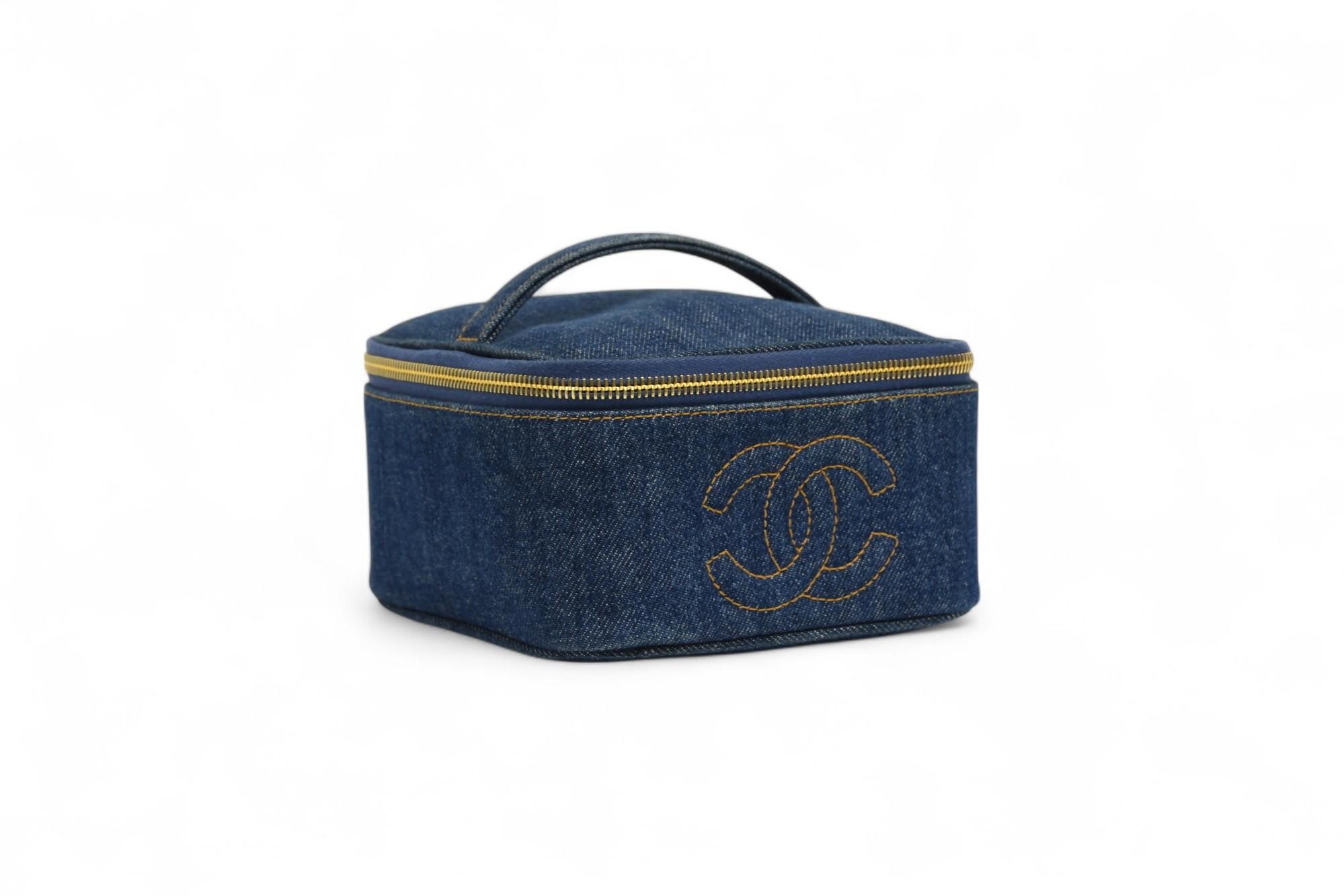 Questo astuccio da viaggio Chanel sfoggia una silhouette raffinata ma giocosa, realizzata in denim lavaggio scuro con impunture dorate a contrasto. Il corpo compatto e morbidamente strutturato presenta un manico superiore arrotondato, una cerniera