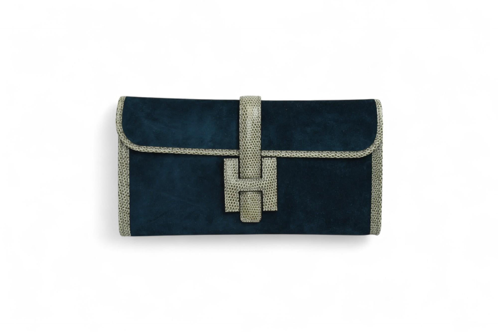 This stunning Hermès Jige Elan 29 clutch is crafted in sumptuous Bleu Ocean Veau Doblis suede, complemented by contrasting natural lizard trim for a bold and luxurious finish. The elongated silhouette is enhanced by the signature 'H' tab closure, a