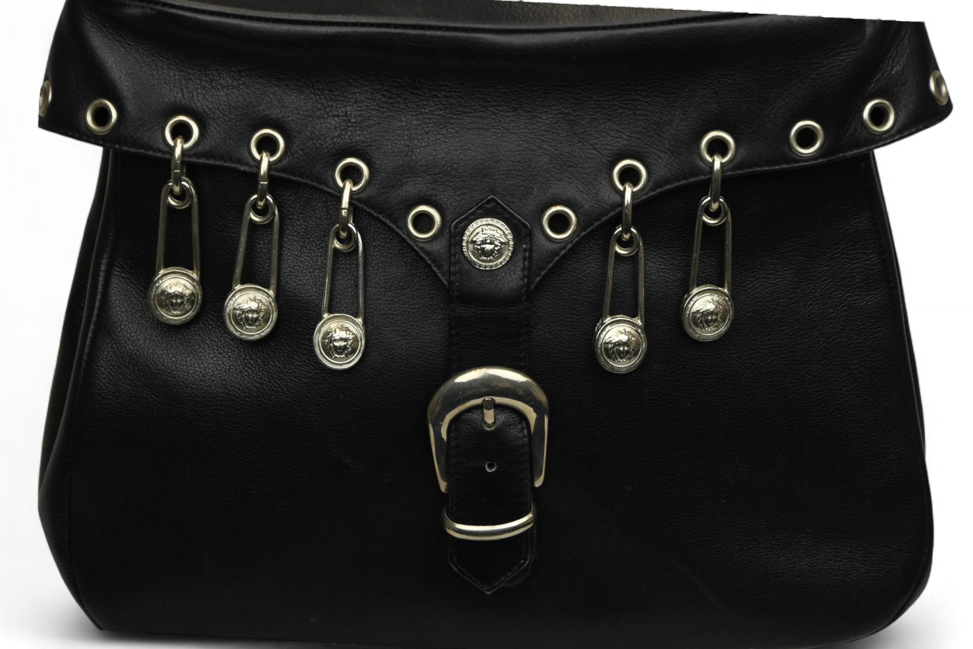 Vestige emblématique des années 1990 de Versace, ce sac à main rare de Gianni Versace allie une attitude punk à des détails opulents. Confectionné en cuir lisse noir, le rabat est orné d'œillets argentés et d'épingles à nourrice estampillées Medusa.