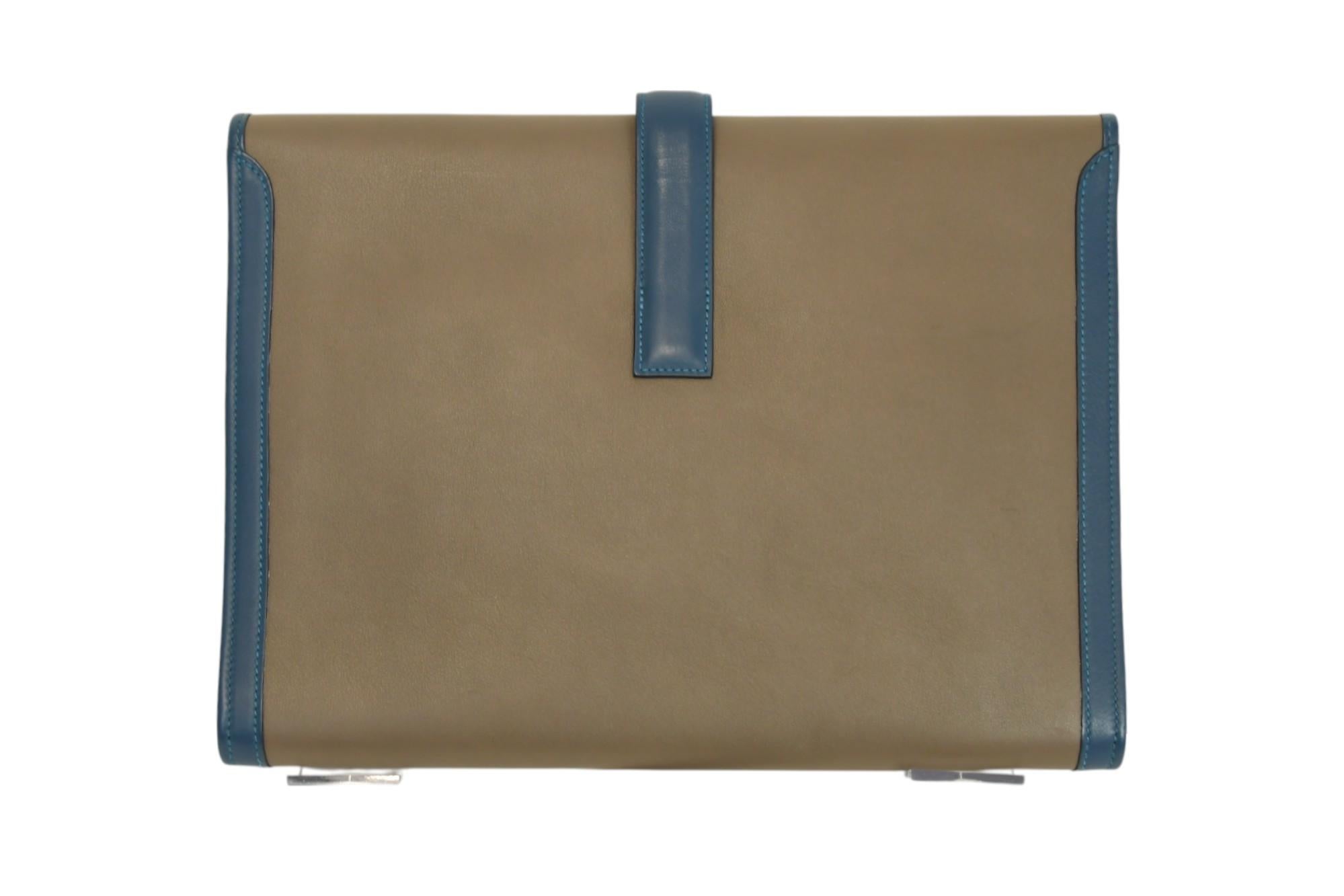 Questa pochette Jige GM di Hermès è un pezzo raffinato in lussuosa pelle color taupe, con rifiniture blu e l'iconica chiusura con cinturino ad 