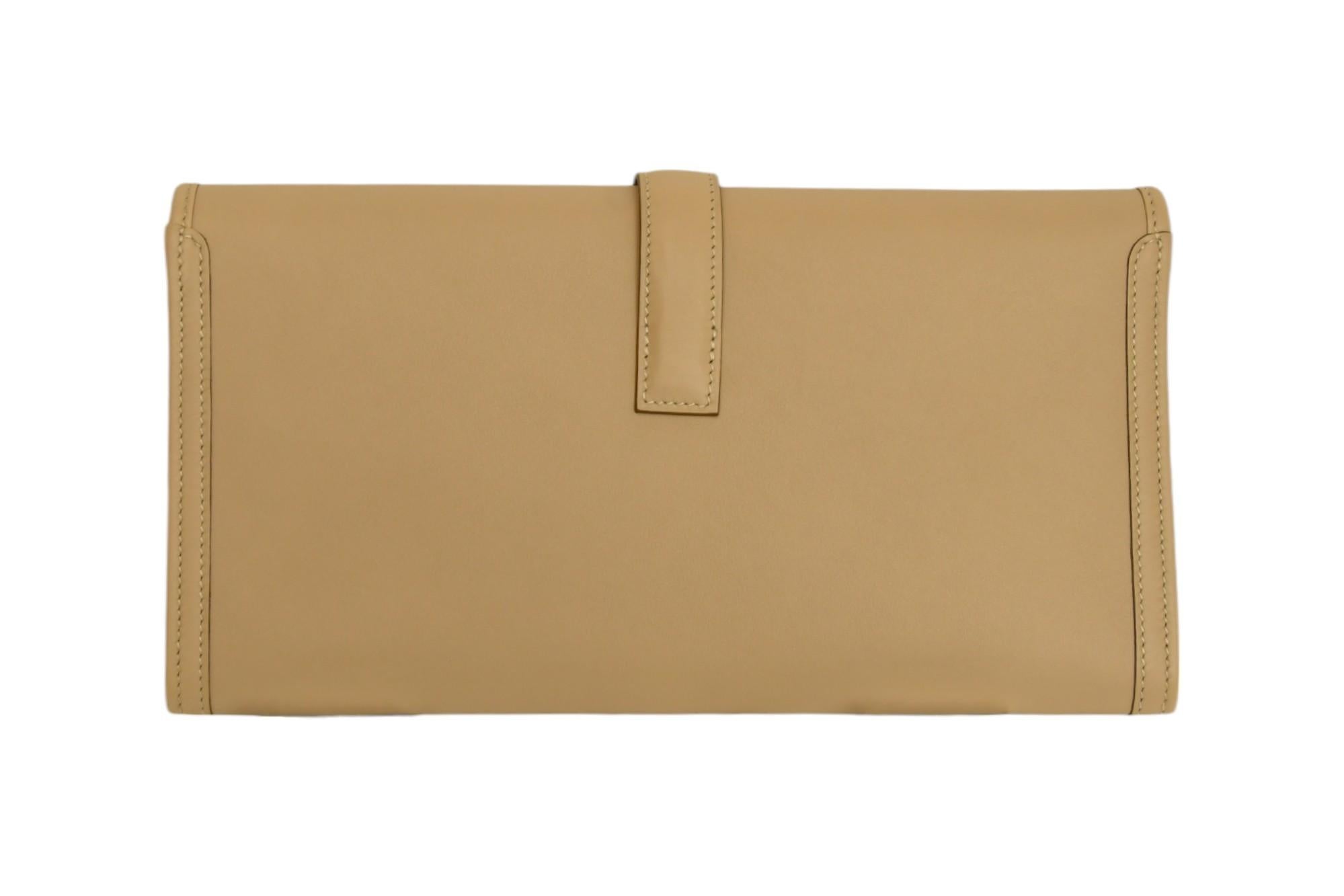 La pochette Hermès Jige PM è l'incarnazione di una tranquilla eleganza, resa qui in una morbida pelle beige che irradia una raffinatezza senza tempo. Il suo design minimalista è accentuato dall'iconica chiusura con linguetta ad 