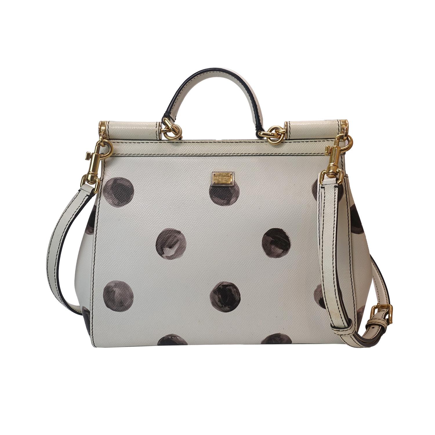 Introduci un'eleganza giocosa nel tuo guardaroba con questa borsa grande Sicily di Dolce & Gabbana in pelle bianca, ornata da pois neri dipinti a mano. Caratterizzata da finiture dorate, chiusura magnetica con bottone a pressione, manico superiore