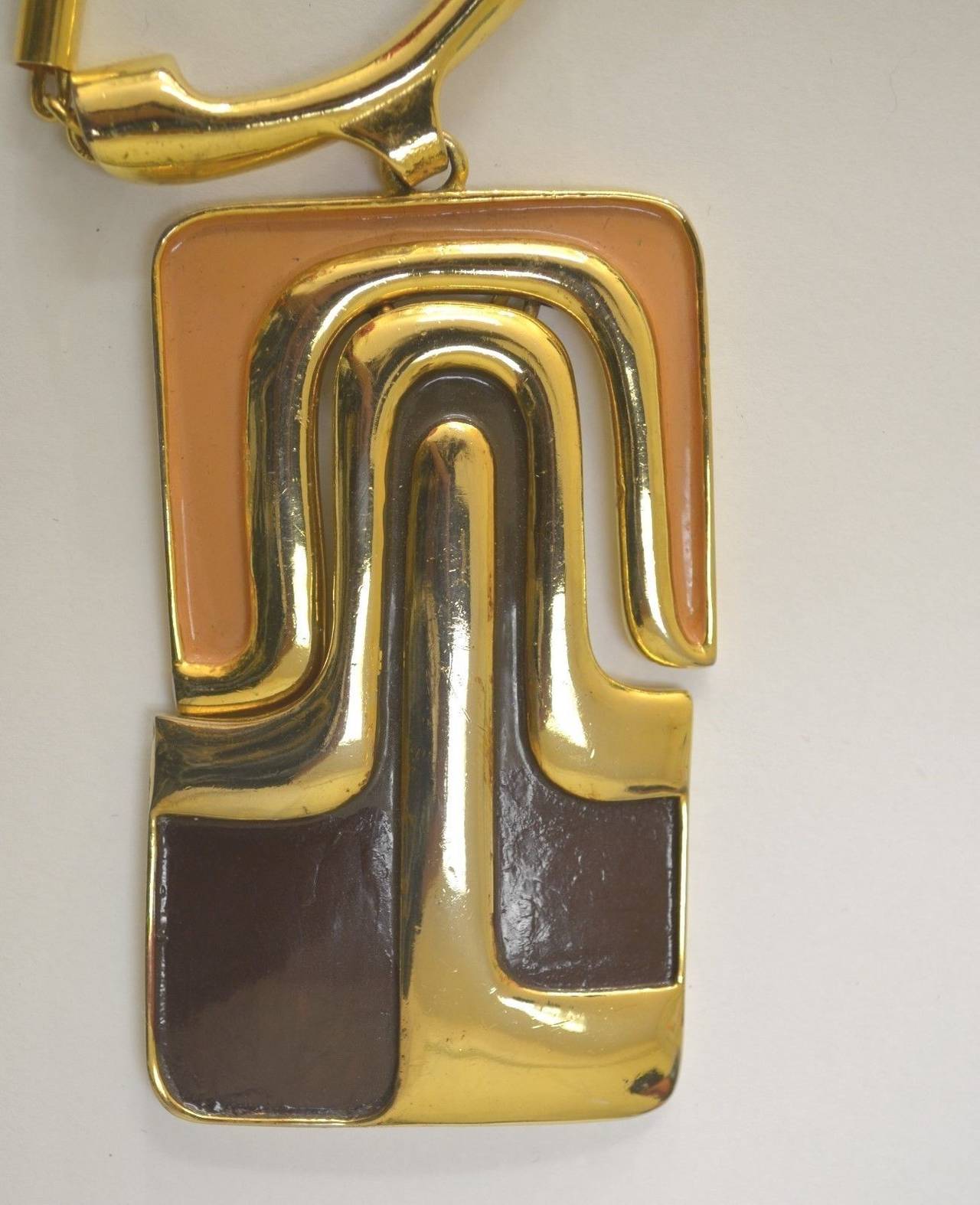 Vintage Pierre Cardin Necklace has a large pendant with brown and peach detail to the gold-tone metal (reticulated moving piece), and tube metal chain with a spring ring closure.

Measurements:
Length - 16'' chain 
Pendant - 3.75'' long
