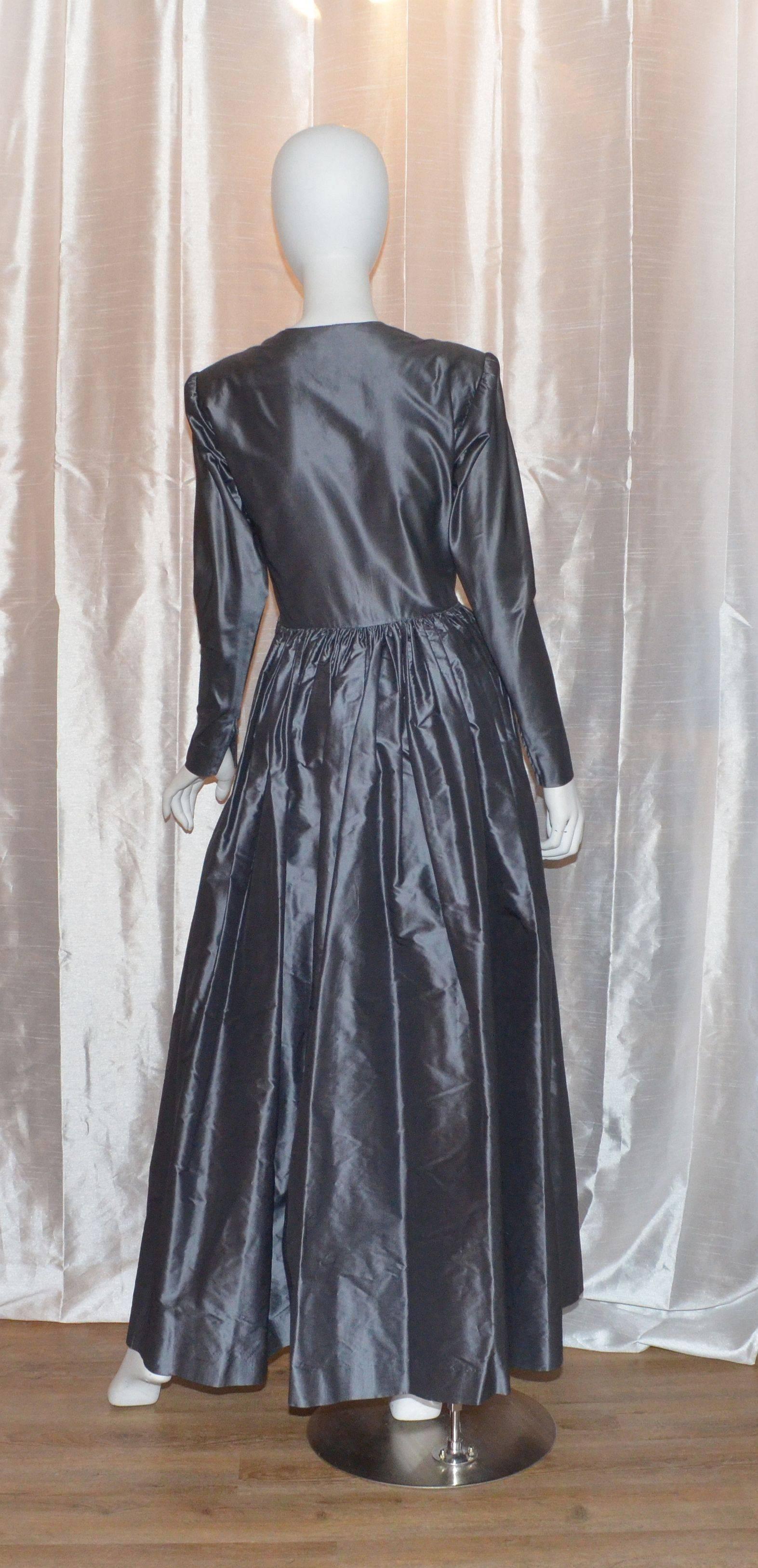 Vintage 1980s Yves Saint Laurent gown is made with a gunmetal-colored lightweight silk taffeta fabric, crossover neckline, gathered waist, and long sleeves which have zippers at the cuffs. Dress has a side zipper closure and pockets at the waist.