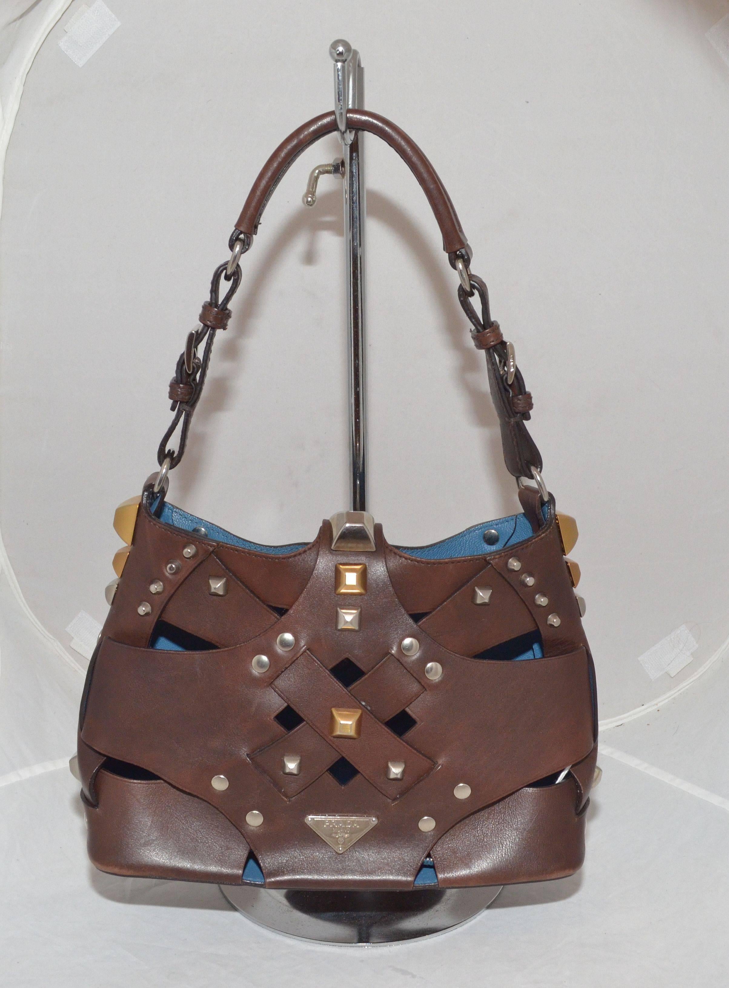 Prada Woven Leather Studded Cutout Mini Handbag

Prada handbag featured in a dark brown leather with gold and silver-tone studding, flap strap with a magnetic closure. There is a decorative buckle on the handle, protective feet at the base, and