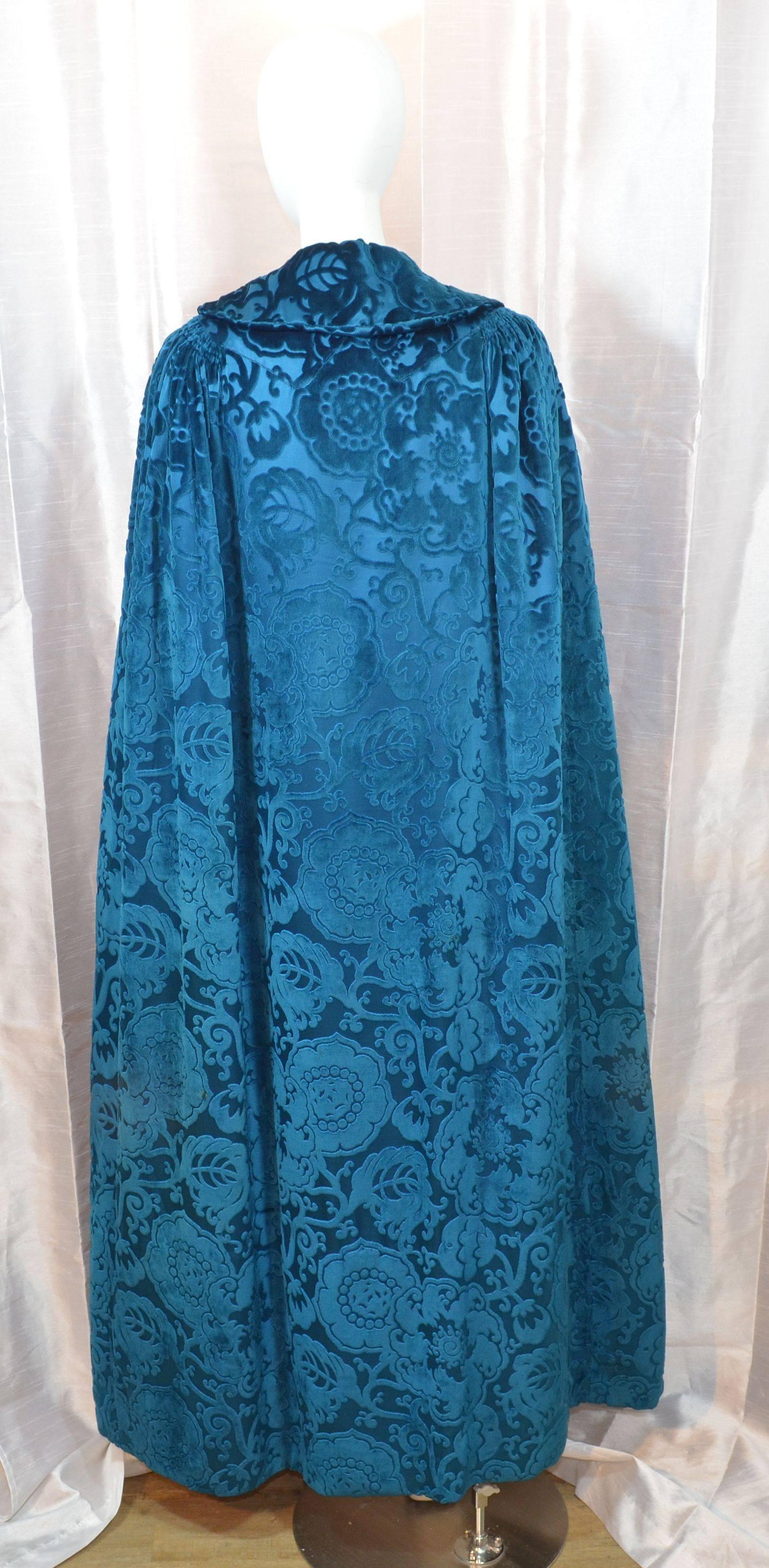 Early 20th century silk velvet cape featured in a beautiful soft royal blue cut velvet with a gold-tone metal filigree hook-and-eye closure at the neck. Fully lined. Cape has a length of 58 inches. Flat across the arm holes : 60 inches. Outer cape