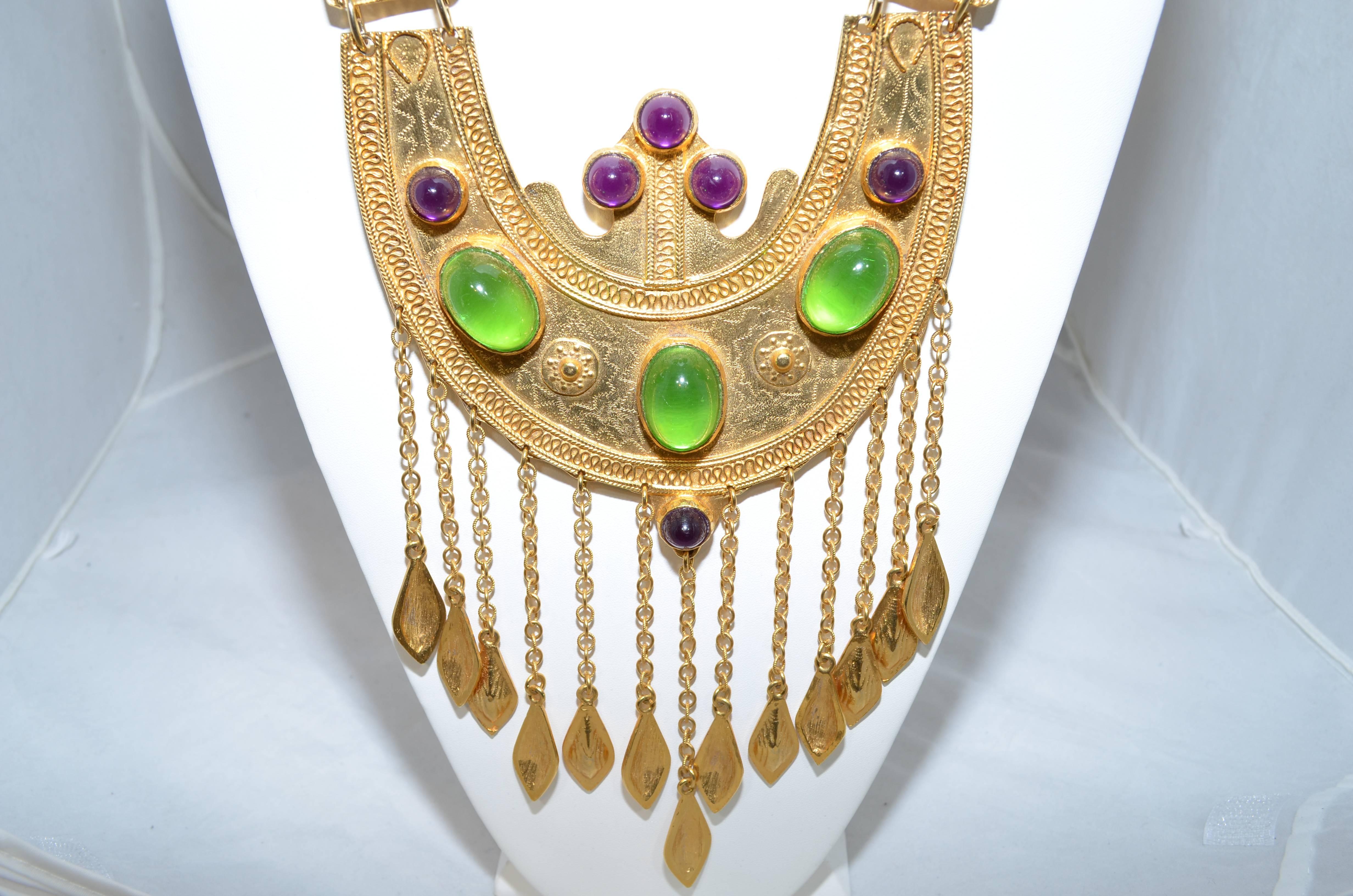 Amazing vintage statement Etruscan style necklace by Alexis Kirk is gold plated and featuring purple and green glass cabochons, with a fringed metal detail. 

American-born Armenian, Alexis Kirk was inspired by symbolism of different cultures and