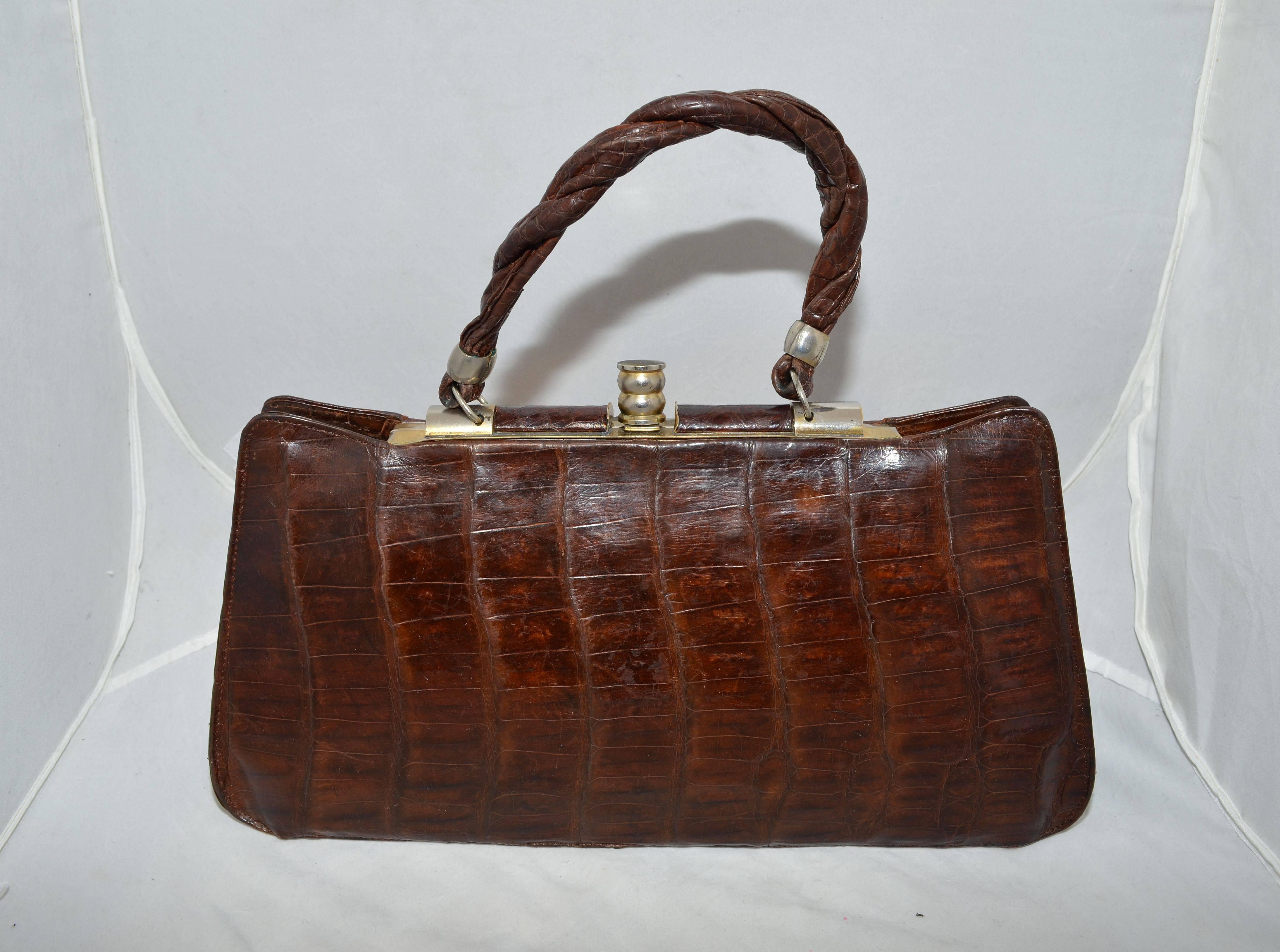 Vintage alligator clutch bag from the 1940's featured in brown with gold-tone brass hardware, twisted alligator strap along the front center and a twisted top handle. Lift clasp closure at the top and fully lined in suede. Interior features four