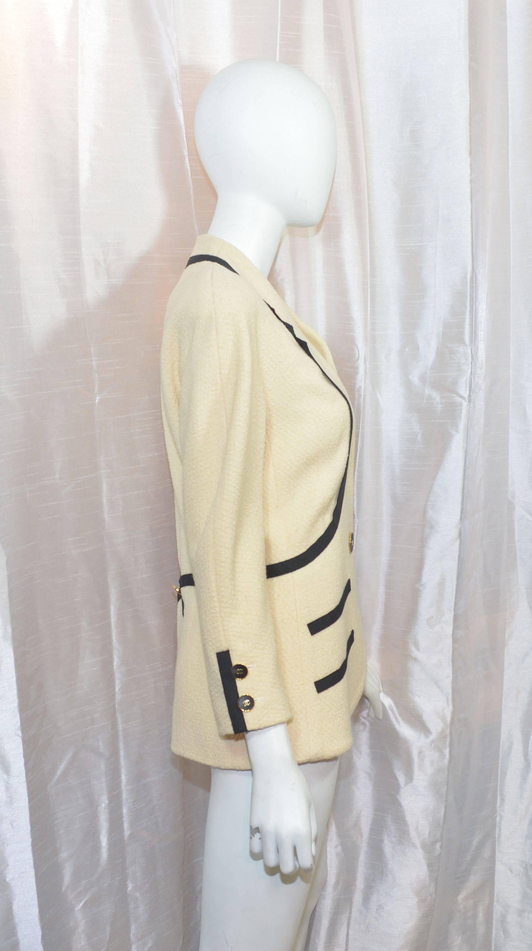 Chanel jacket from collection 25 in 1991. Featured in an ivory knit with black ribboning, one center button closure and buttons along the cuff. Ribbon detail continues to the back of the jacket with a button finish. Made with 100% wool and lined in