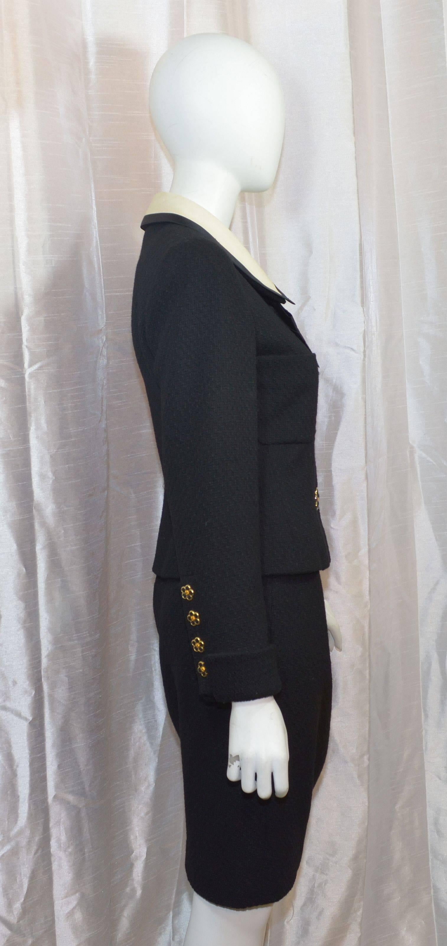 Chanel skirt suit from collection 25 from 1991. Suit jacket features gold-tone and black flower button closures along the front and on the cuffs, two slip pockets at the bust, satin bow tie at the neck, and a removable ivory satin collar. Skirt has