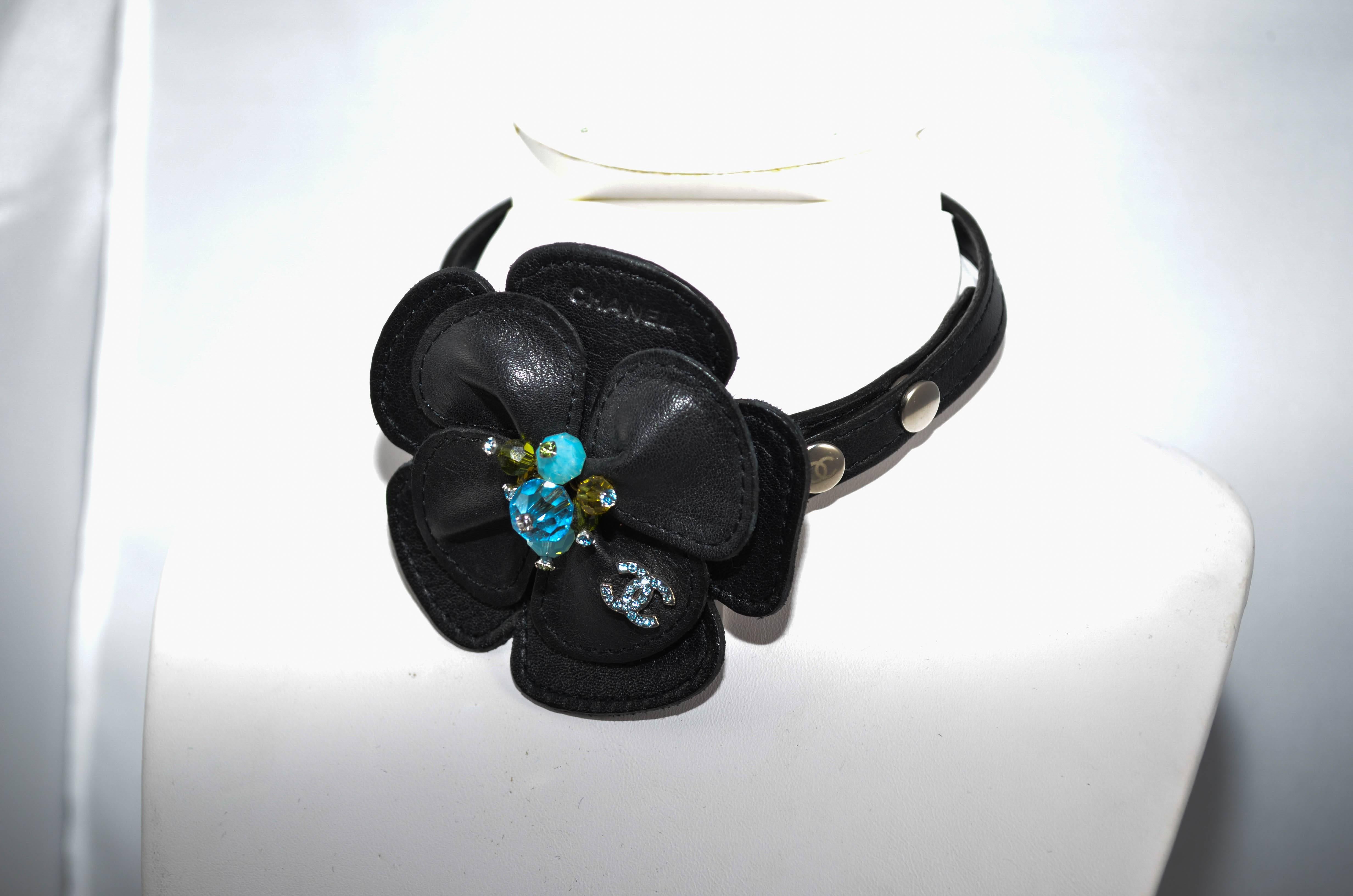 Rare and fabulous Chanel black leather camelia flower choker featuring a three button snap closure, blue and green crystal beads at the center of the flower tipped with blue and green rhinestones, and Chanel's signature CC with silver hardware and