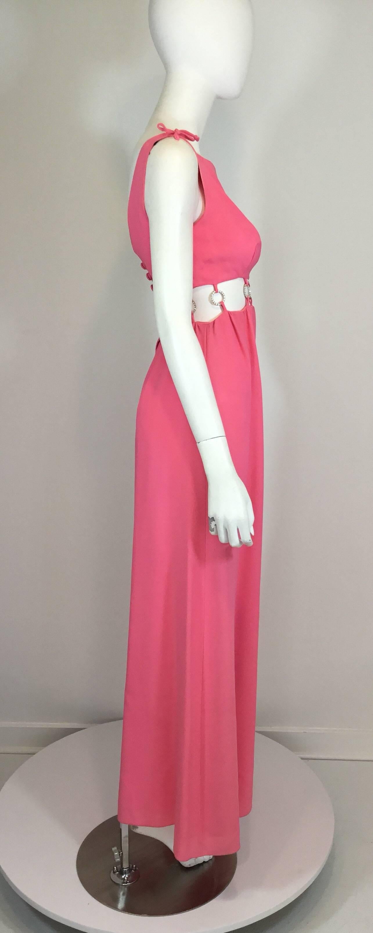 Vintage 1960's maxi dress in a pink crepe-like fabric with an exposed midriff that features decorative rhinestone O-rings connecting the top and skirt. Dress is fully lined with a low backline and a zipper fastening. Excellent condition.