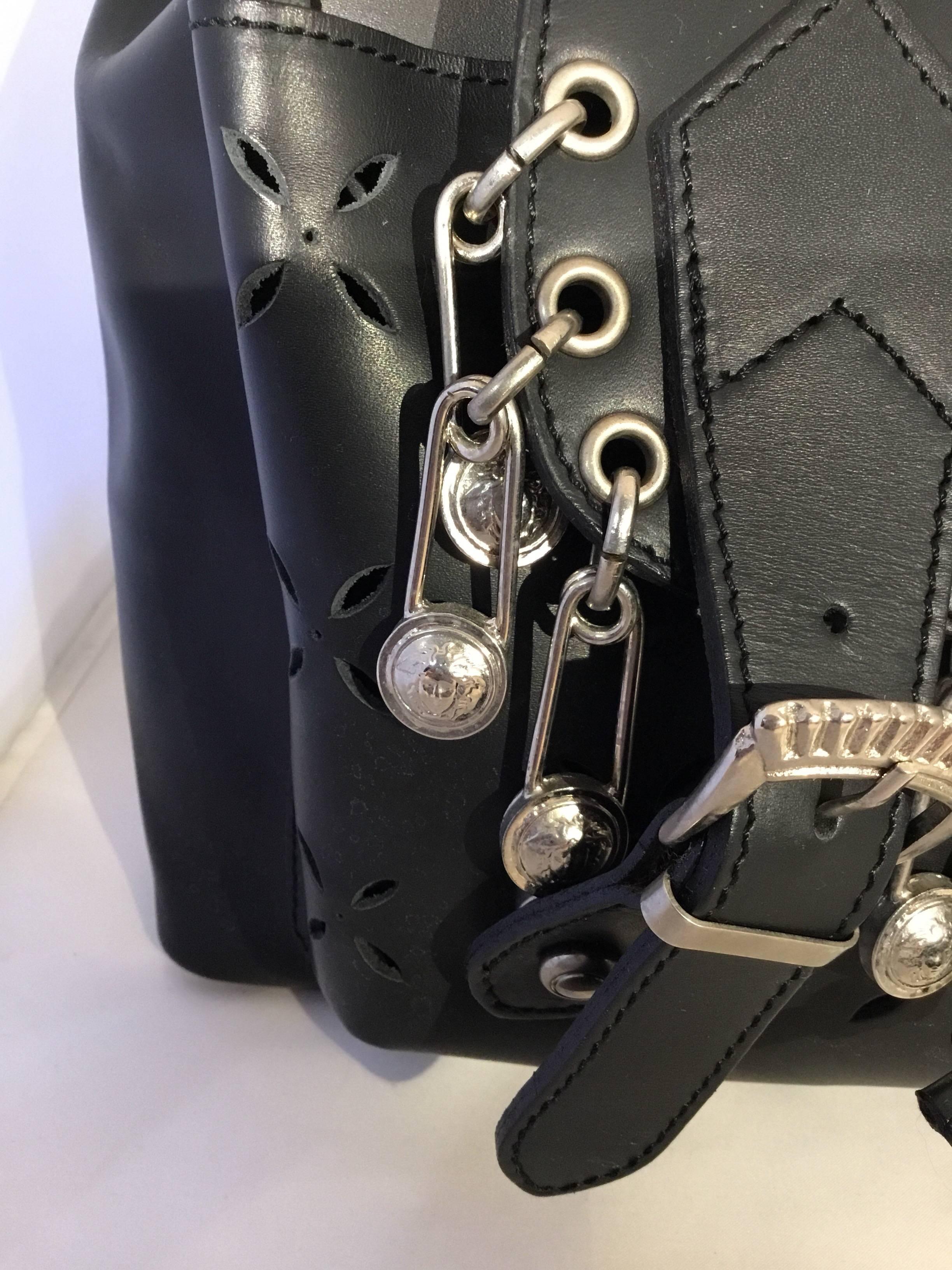 Gianni Versace Vegan? faux leather backpack features laser cut detailing, a flap closure with silver-tone rivets along the trim and dangling Medusa safety pins, flap closure also has decorative buckles in which are disguised as magnetic snap