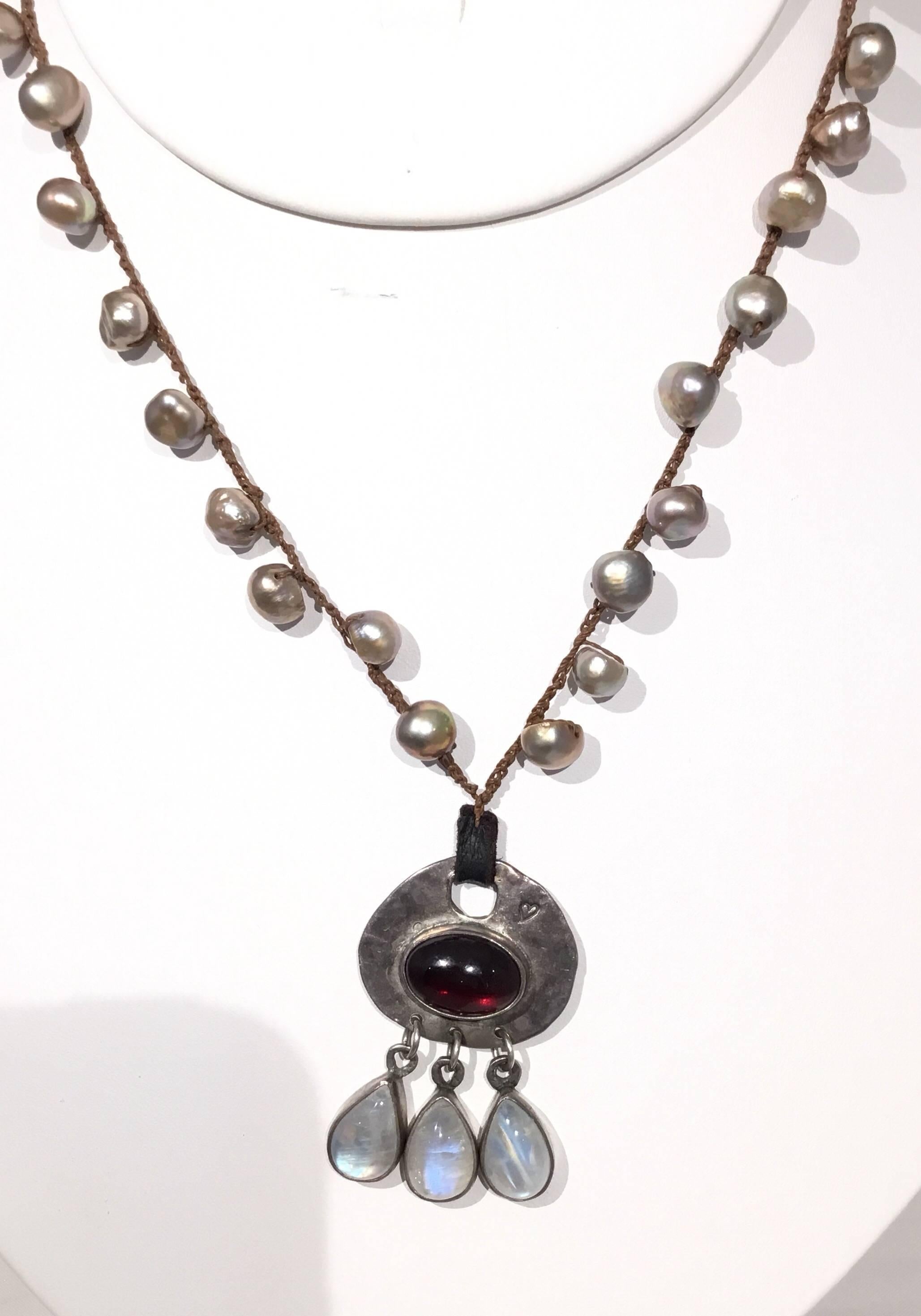 Jes Maharry knotted string necklace with pearls throughout, silver clasp, pendant is sterling silver with a garnet stone at the center and dangling moonstone gems. Approximate length 9 inches drop or 18
