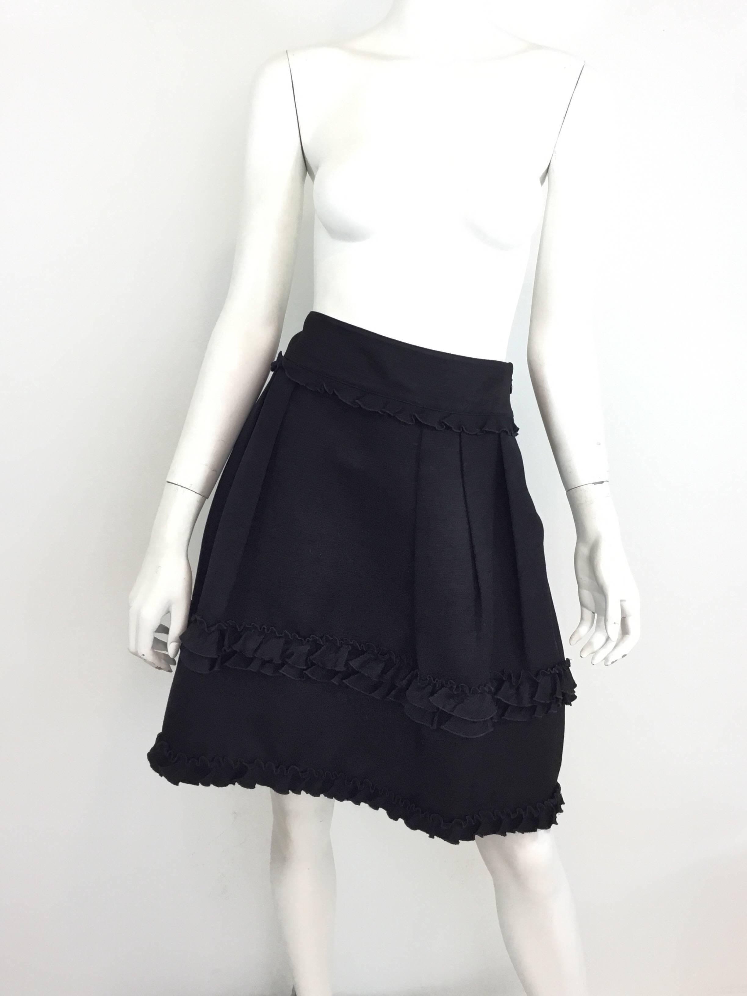 Valentino skirt and jacket set featured in black silk blend fabric. Jacket has a single hook-and-eye fastening, faux slip pockets at the bust, and a ruffle-like trim. Skirt has a tiered ruffle hem and a side zipper fastening. Labeled size 8, made in
