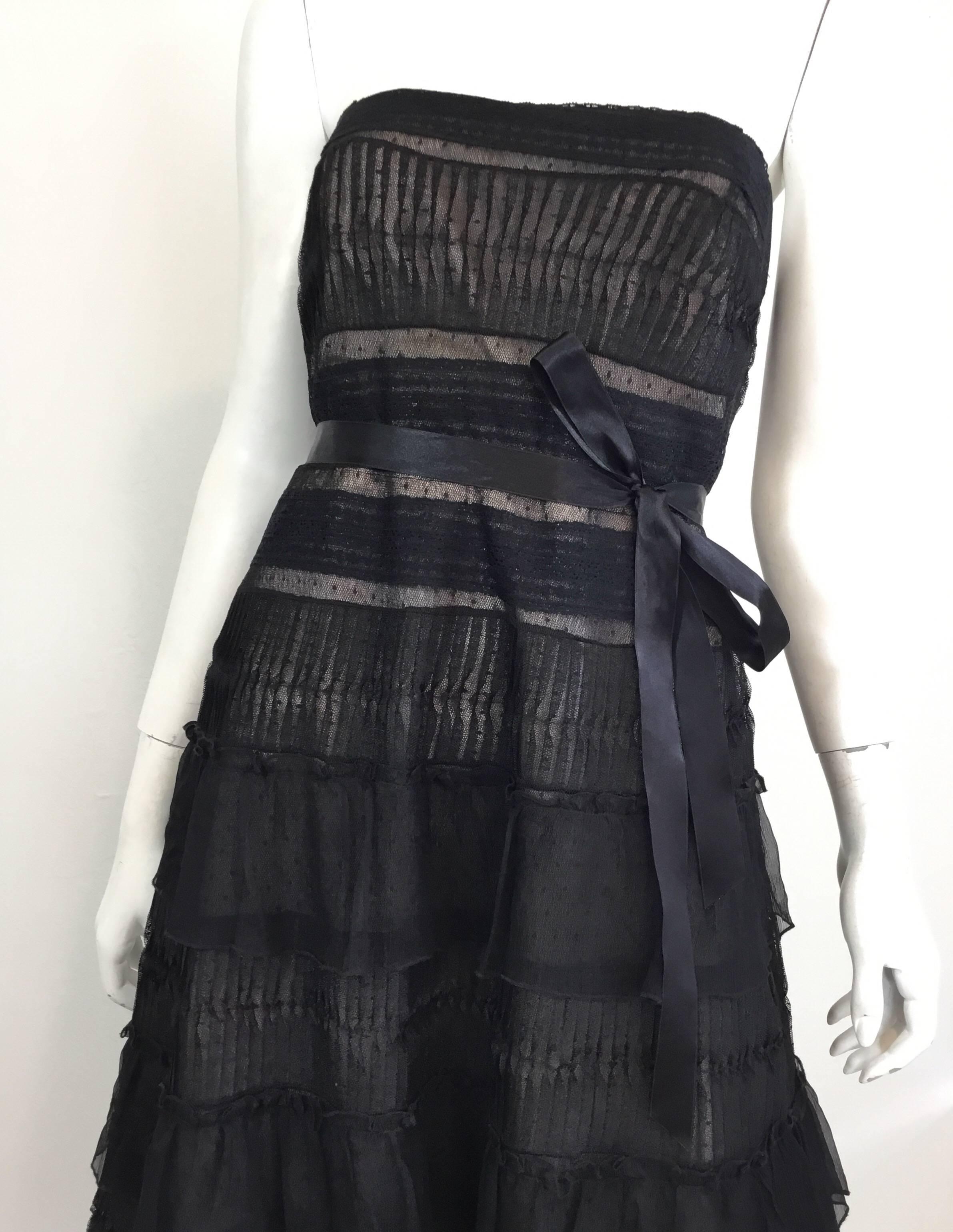 Carolina Herrera dress in black lace features a strapless style with a back zipper and ribbon waist tie fastening, silk sheer tiered detail, and an ostrich feather hem. Dress is fully lined. 

Measurements:
bust 34'', waist 30'', hips 40'', length