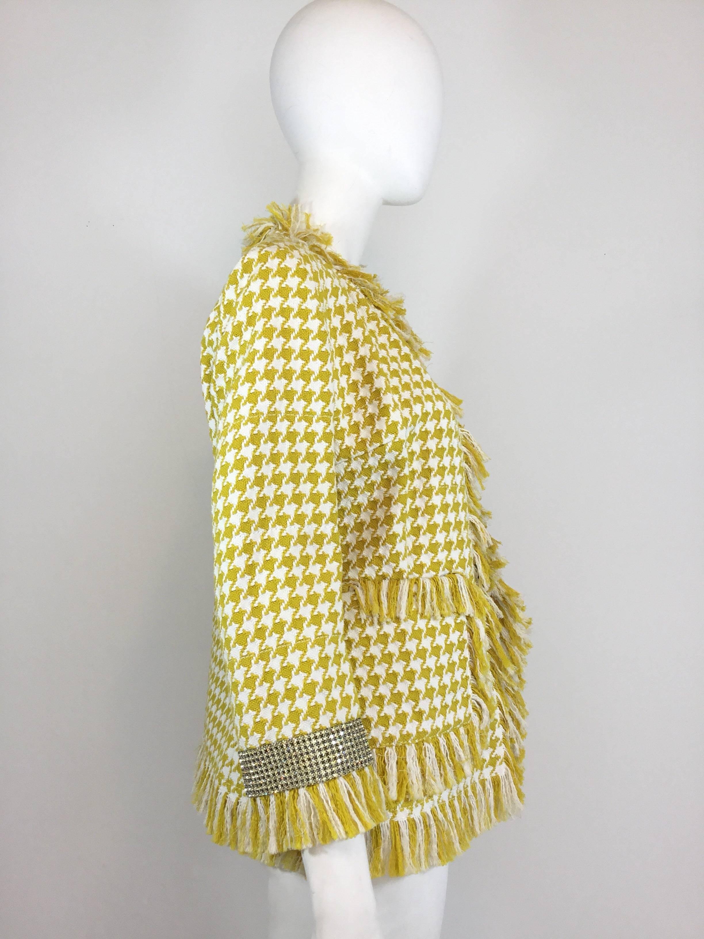 Yellow and white houndstooth Dolce & Gabbana jacket features a houndstooth knit pattern throughout, fringed trimming, and crystal cuffs. Lined in leopard print silk chiffon. Jacket has hook-and-eye clsoures, full silk leopard print lining. Labeled