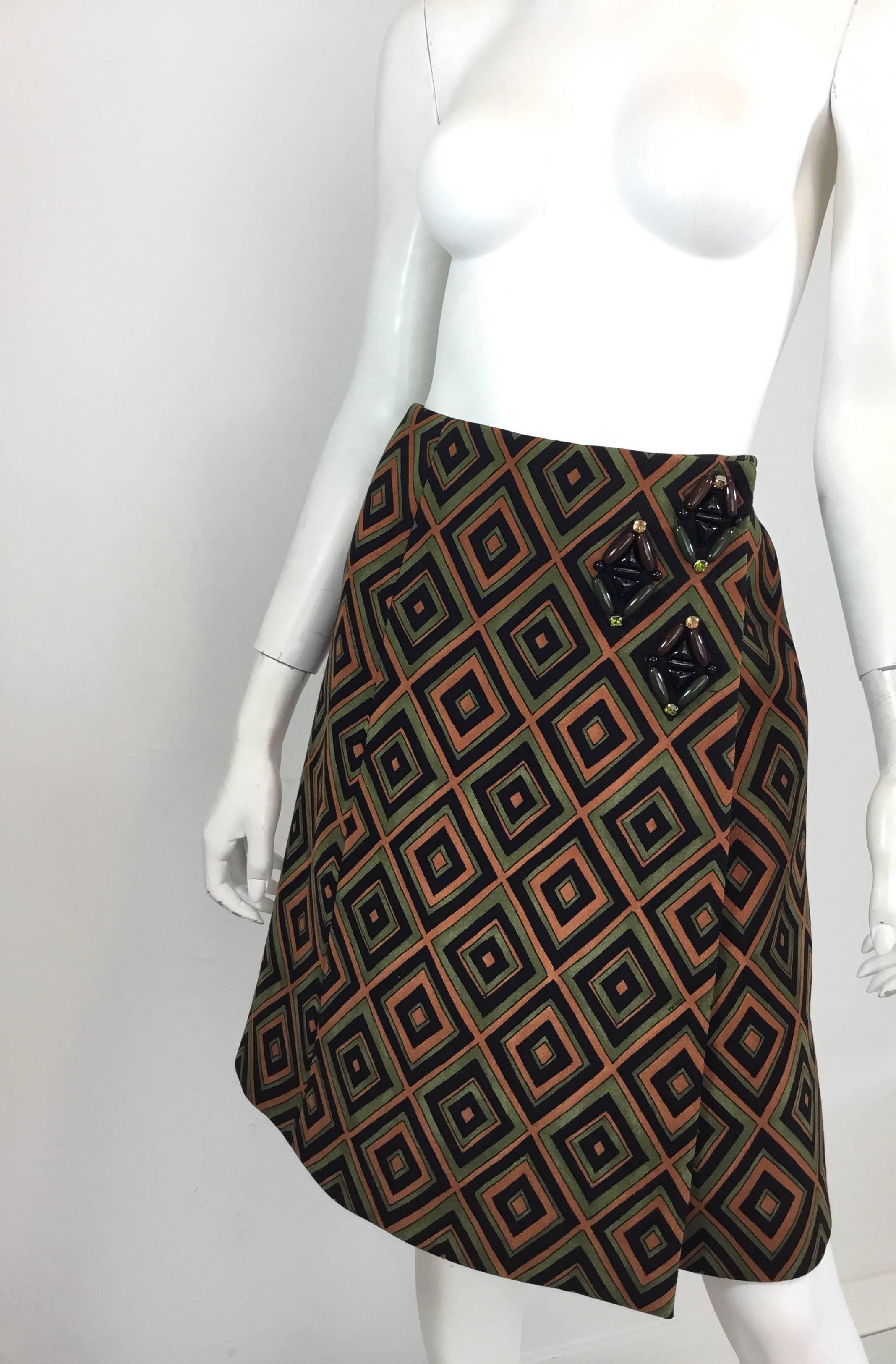 Prada skirt from the Fall 2012 RTW Collection inspired by the house’s Fall/Winter 1996 Collection — features an olive green, brown, and black diamond geometric print with bead and rhinestone embellishing at the left hip. Skirt has snap studs and
